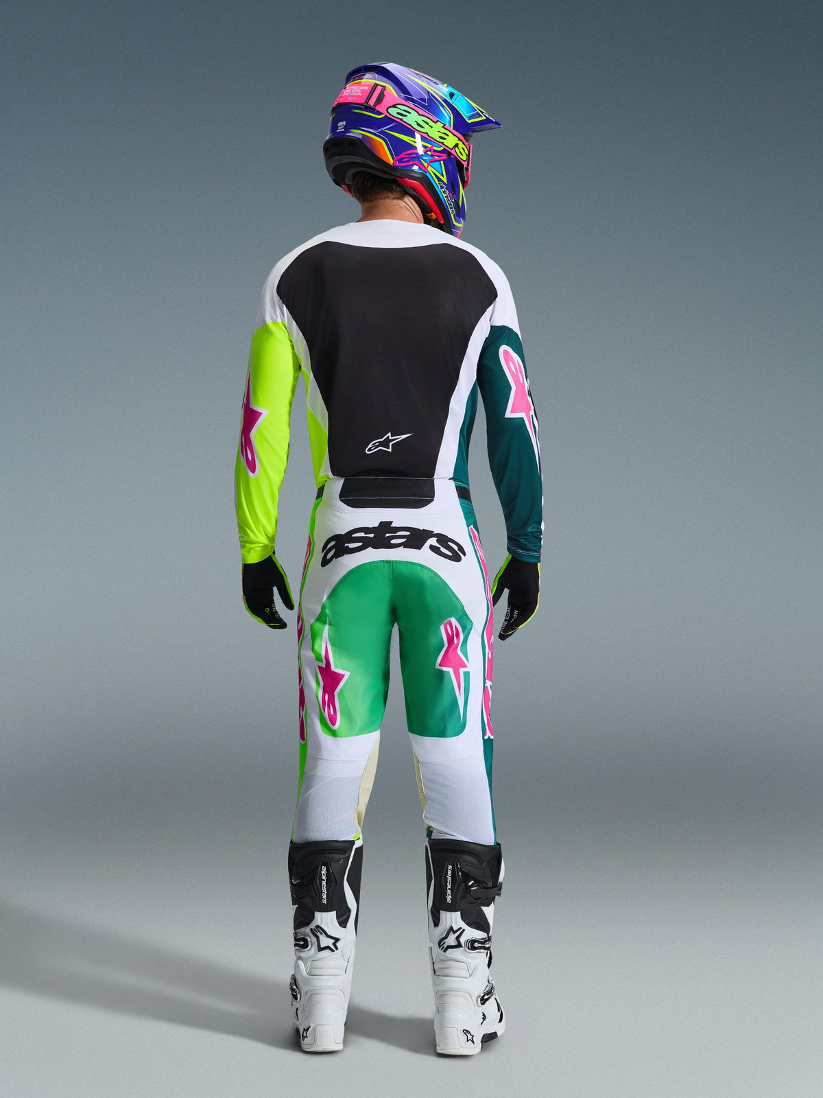 Motocross-Fahrer in der Rückansicht, trägt das 2026 Racer Portl Trikot in Green White Black, mit schwarzer Rückenpartie und asymmetrischen grünen Ärmeln mit pinkfarbenen Stern-Logos, kombiniert mit passender Motocross-Hose und weißen Stiefeln.