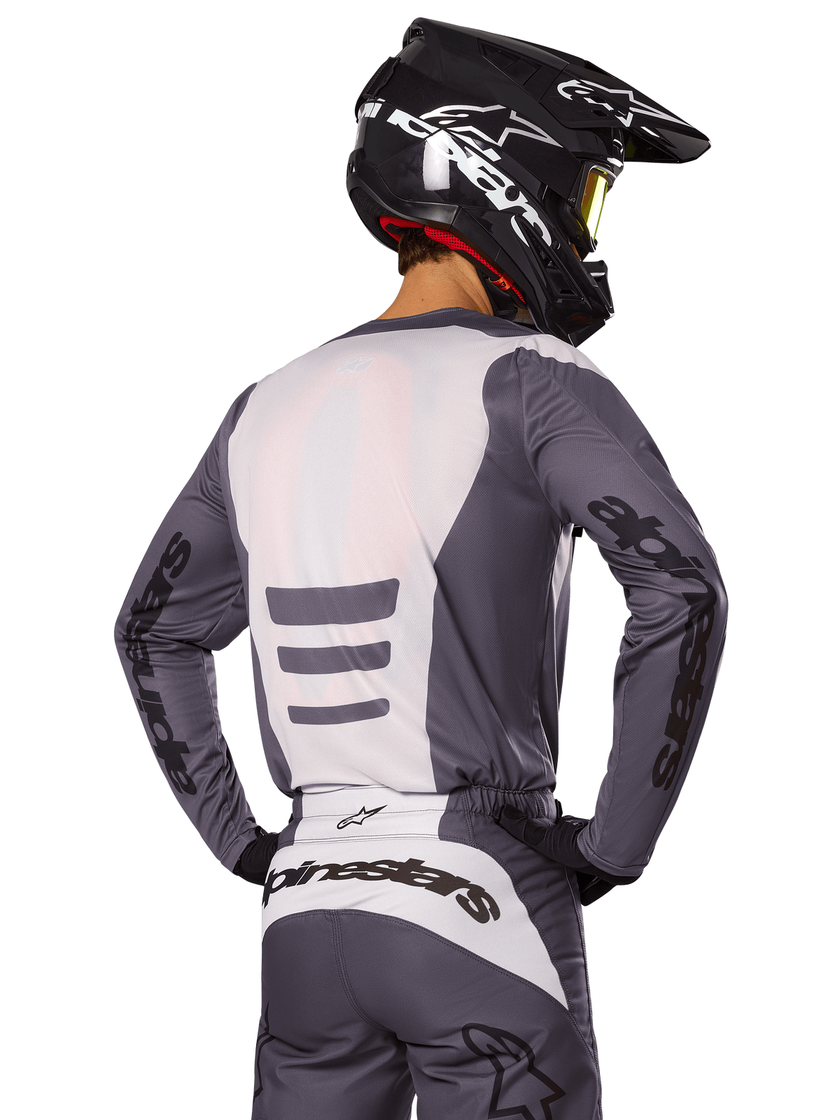 Motocross rider from behind wearing Alpinestars 2025 Fluid Haul Gear Set, Gray and White jersey and pants, black helmet with white graphics, yellow goggles, coordinated motocross racing outfit