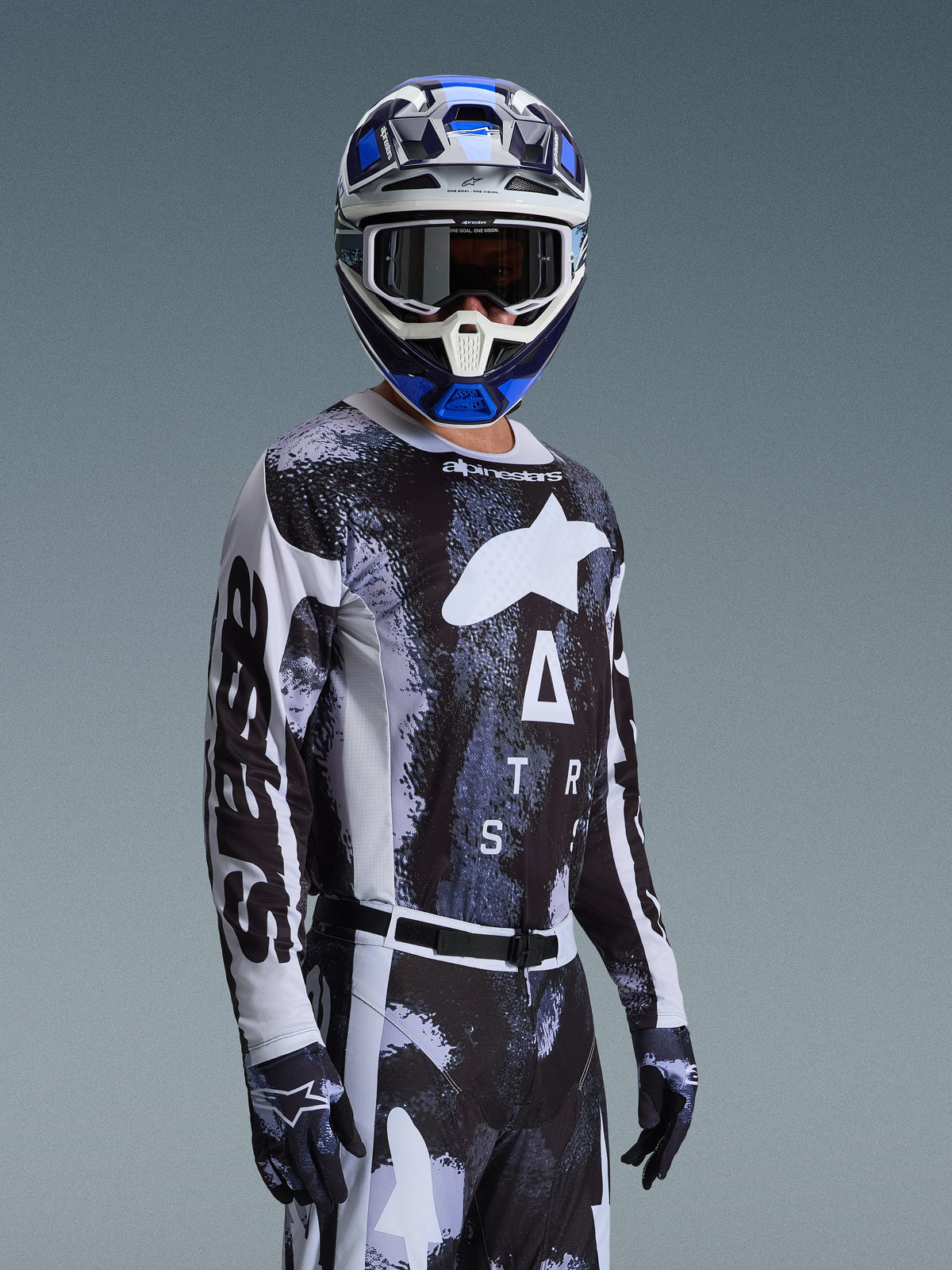 Motocross-Fahrer im Alpinestars 2026 Racer Lahnd Jersey in Iron Camo, mit einem schwarz-grauen Camouflage-Muster und einem großen weißen Alpinestars-Logo auf der Brust, kombiniert mit einem passenden Helm und Handschuhen für den Offroad-Rennsport.
