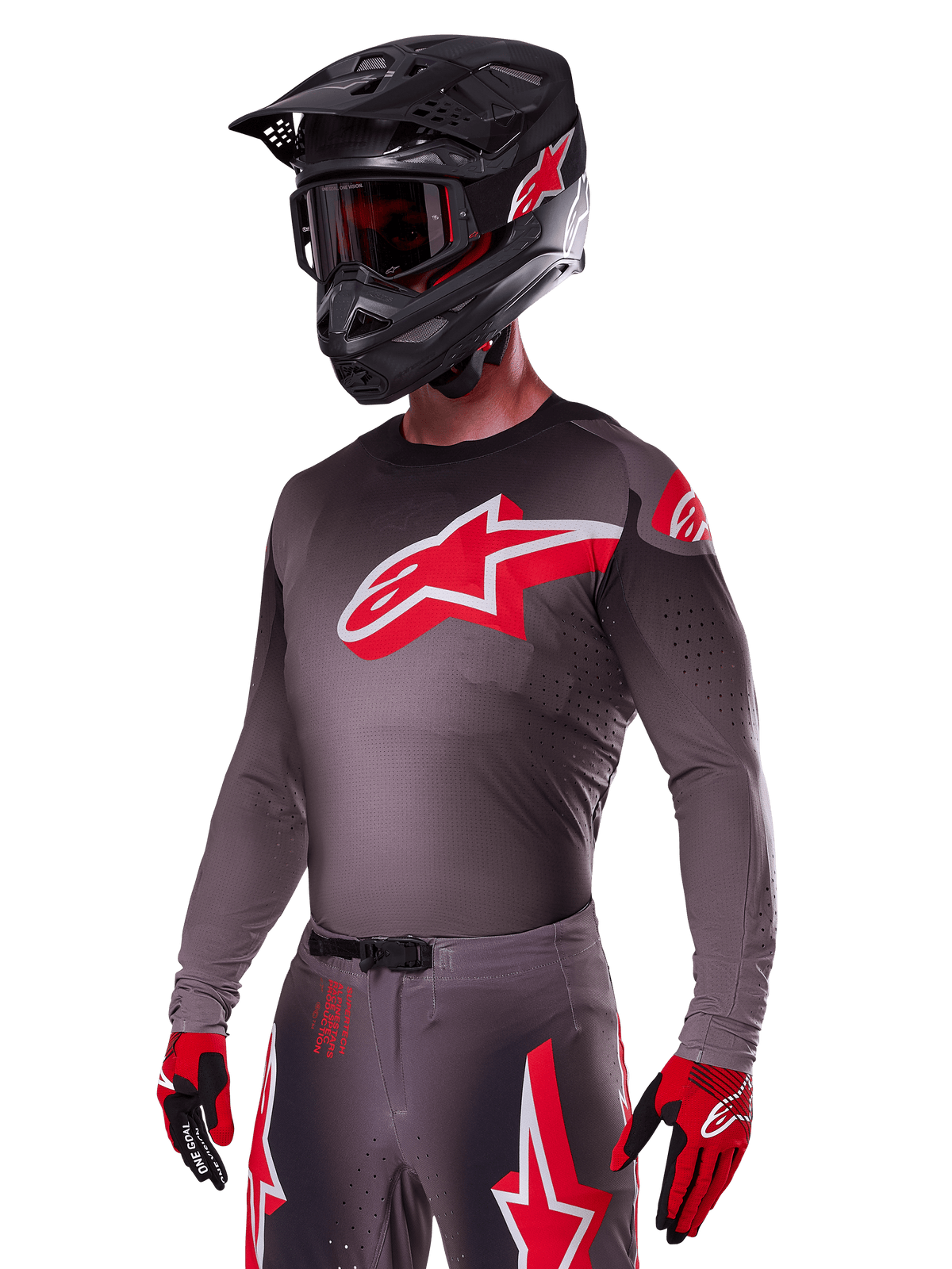 Alpinestars 2025 Supertech Lipan Gear Set, Motocross rider wearing a dark grey jersey and pants with red and white accents, featuring a large red Alpinestars logo on the chest, laser-cut perforations for ventilation, matching black helmet, red goggles, and red and black gloves.