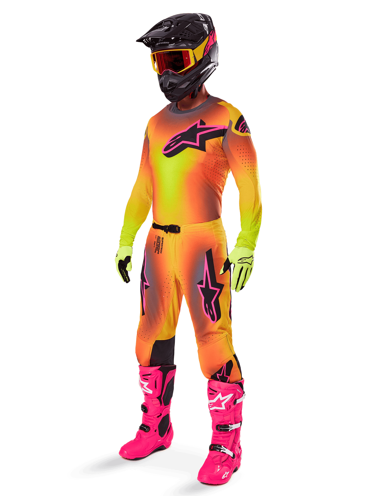 Motocross rider wearing the 2025 Alpinestars Supertech Lipan Gear Set, yellow and orange gradient jersey and pants with pink accents, black helmet with yellow-red goggles, bright yellow gloves, and vibrant pink boots, coordinated off-road racing outfit