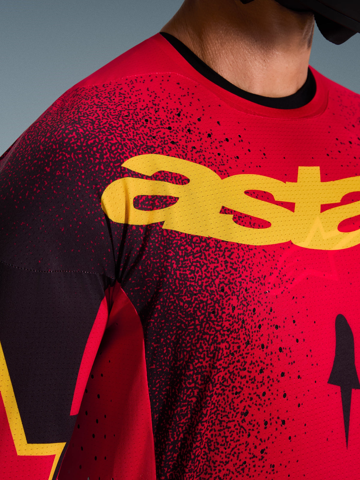 Alpinestars 2026 Supertech Scenz Trikot, Motocross-Trikot, Rot, Schwarz und Gelb, Nahaufnahme des Brustbereichs mit gelbem Branding, schwarzem Sprenkelmuster und lasergeschnittenen Perforationen zur Belüftung.