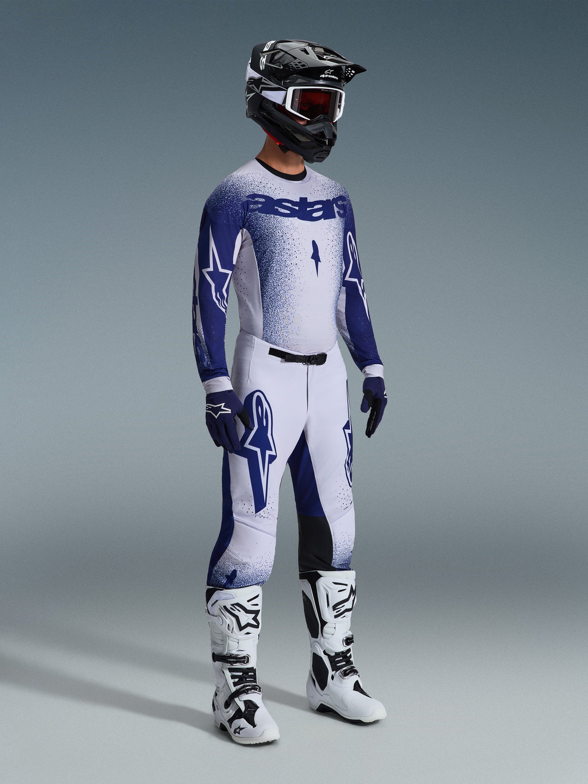 Motocross-Fahrer in kompletter professioneller Rennausrüstung, 2026 Supertech Scenz Trikot in Hellgrau und Dunkelblau, passende Motocross-Hose mit Stern-Grafiken, schwarzer Helm mit roter Brille, weiß-schwarze Performance-Stiefel, farblich abgestimmte blau-weiße Handschuhe für Offroad-Rennen