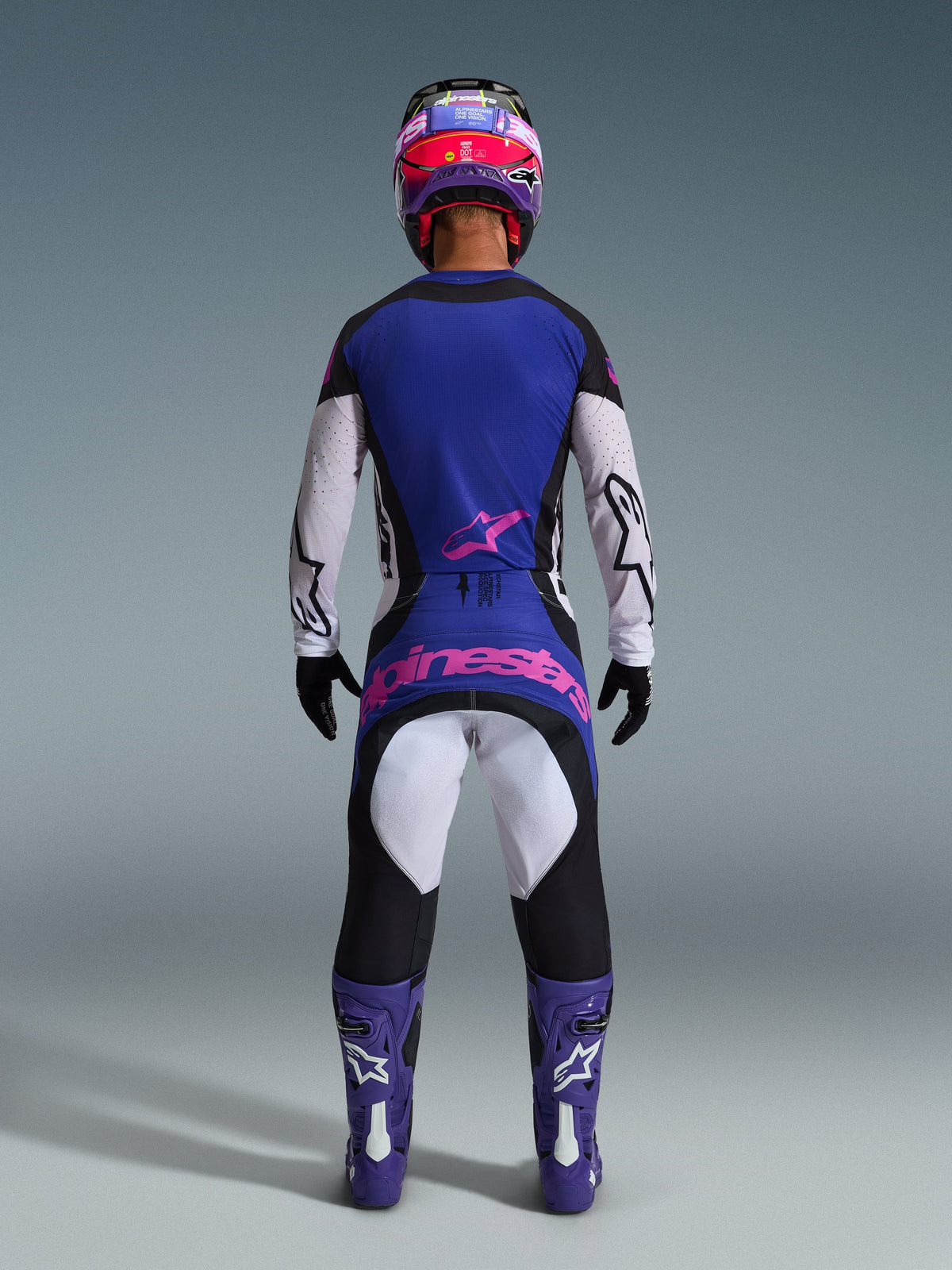Motocross rider viewed from the back wearing the 2026 Techstar Knif Jersey, Black Light Gray Purple, matching motocross pants with pink branding, purple boots and helmet, coordinated high-performance off-road gear