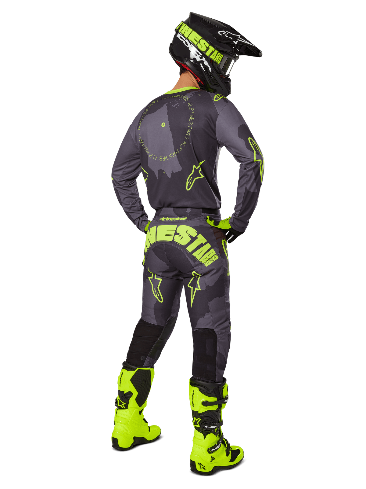 Motocross-Fahrer in der Rückansicht im Alpinestars 2025 Racer Hollow Trikot und der Hose in Dark Camo Yellow Fluo, mit einem dunkelgrauen Camouflage-Muster und neongelben Akzenten, kombiniert mit einem passenden schwarz-gelben Helm und leuchtend neongelben Stiefeln.