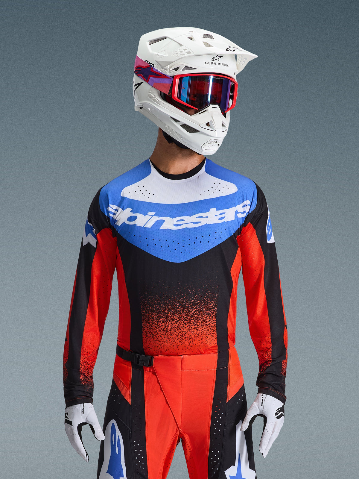 Alpinestars 2026 Techstar Knif Gear Set, Motocross-Rennausrüstung mit einem blau, weiß, schwarz und roten Jersey mit Alpinestars-Branding, passender rot-schwarzer Hose, kombiniert mit einem weißen Helm, roter Goggle und weißen Handschuhen, athletische Performance-Passform für den Offroad-Wettkampf