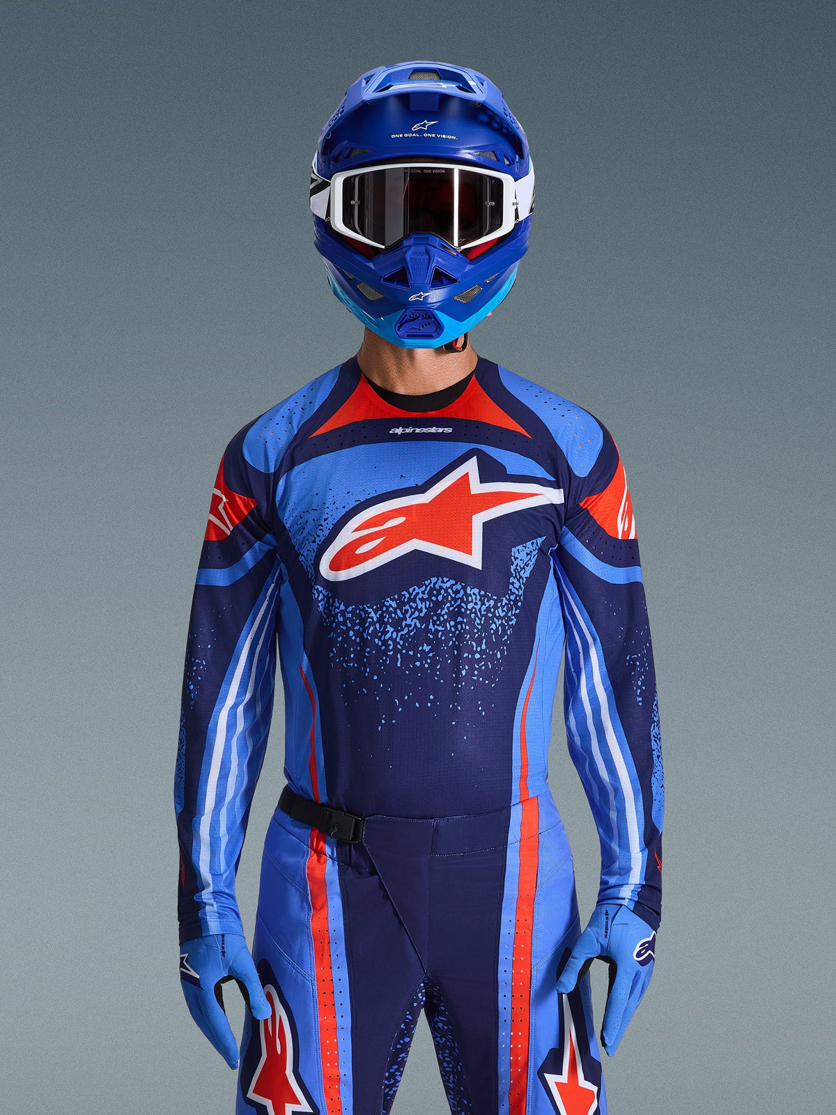 Alpinestars 2026 Techstar Nomur Trikot, Motocross-Renntrikot, Dunkelblau, Orange und UCLA-Blau, getragen mit passender Hose, blauem Helm und Handschuhen, mit weißem Stern-Logo auf der Brust, dynamischen Linien und gesprenkelten Mustern