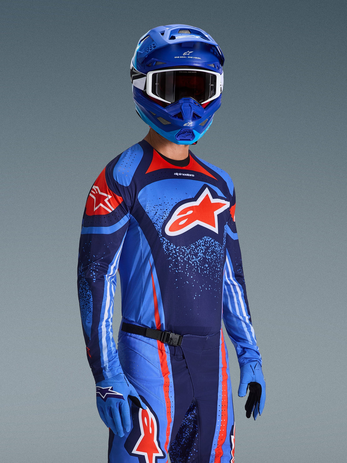 Alpinestars 2026 Techstar Nomur Gear Set, Motocross-Trikot und -Hose in Dunkelblau, Orange und UCLA-Blau, getragen von einem Fahrer mit passendem blauem Helm und Handschuhen, mit markanten Logo-Grafiken und athletischer Rennpassform.