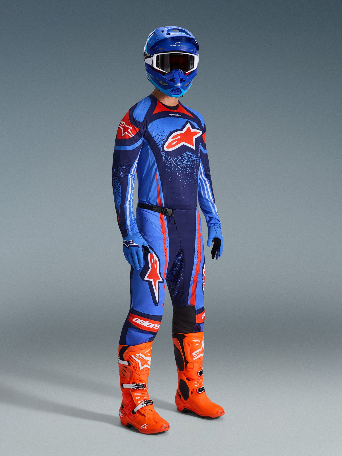 Motocross rider wearing complete racing gear, blue and dark navy Techstar Nomur Jersey with orange Alpinestars logo, matching blue and navy pants with orange accents, blue helmet with white goggles, bright orange boots, and blue gloves, coordinated outfit for off-road racing