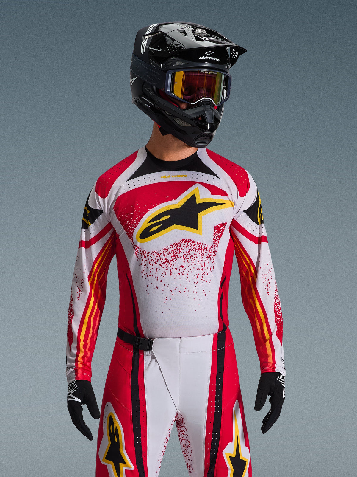 Alpinestars 2026 Techstar Nomur Gear Set, Motocross-Fahrer mit rot-weiß-schwarzem Jersey mit gelbem Logo, passende Hose mit gesprenkeltem Muster, schwarzer Helm und Schutzbrille, schwarze Handschuhe, komplette Rennausrüstung für Offroad-Wettbewerbe
