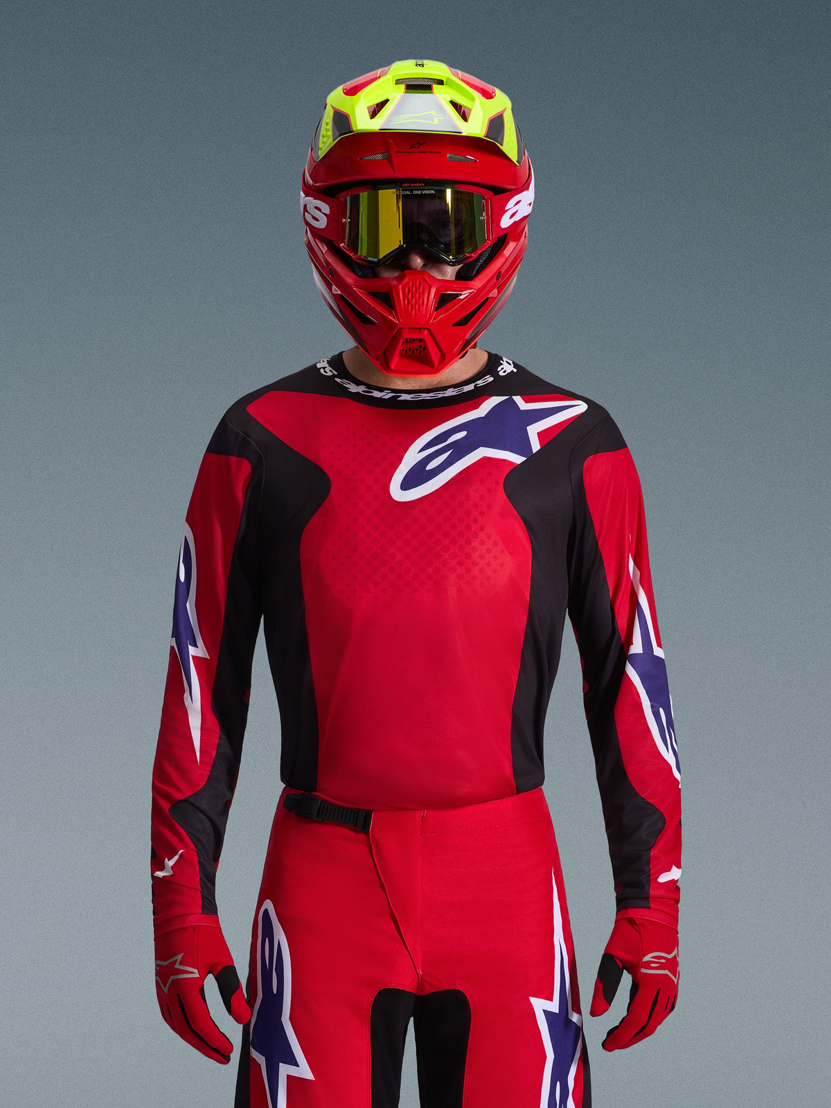 Motocross-Fahrer im Alpinestars 2026 Fluid Grid Gear Set, rotes Trikot mit schwarzen Seiteneinsätzen und weißem Stern-Logo, passende rote Hose und Handschuhe, rot-gelber Helm mit gold getönter Brille, Hochleistungs-Rennausrüstung für Offroad