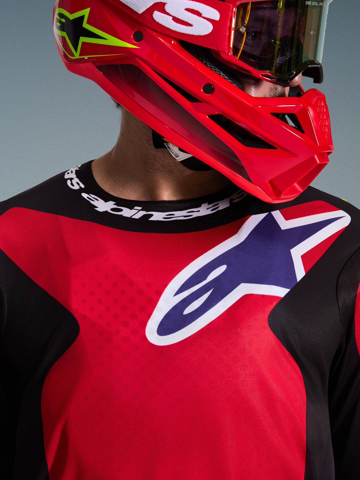 Alpinestars 2026 Fluid Grid Trikot, Rot Schwarz Lila, Motocross-Fahrer trägt das Trikot mit passendem rotem Helm und Brille, großes weiß-lila Logo auf der Brust, Sportkragen mit Alpinestars-Branding, technische Offroad-Rennausrüstung