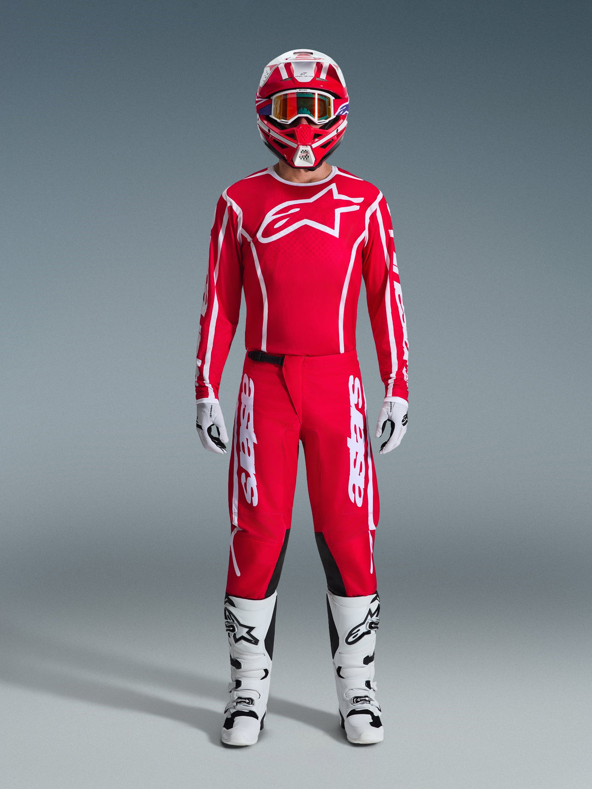 Motocross-Fahrer in kompletter 2026 Fluid Apex Rennausrüstung, rotes Trikot mit weißem Alpinestars-Logo und Branding an den Ärmeln, dazu passende rote Hose mit weißen Akzenten und schwarzen Einsätzen, rot-weißer Helm mit verspiegelter Brille, weiß-schwarze Stiefel und weiß-schwarze Handschuhe, professionelles Ausrüstungsset für Offroad-Performance.