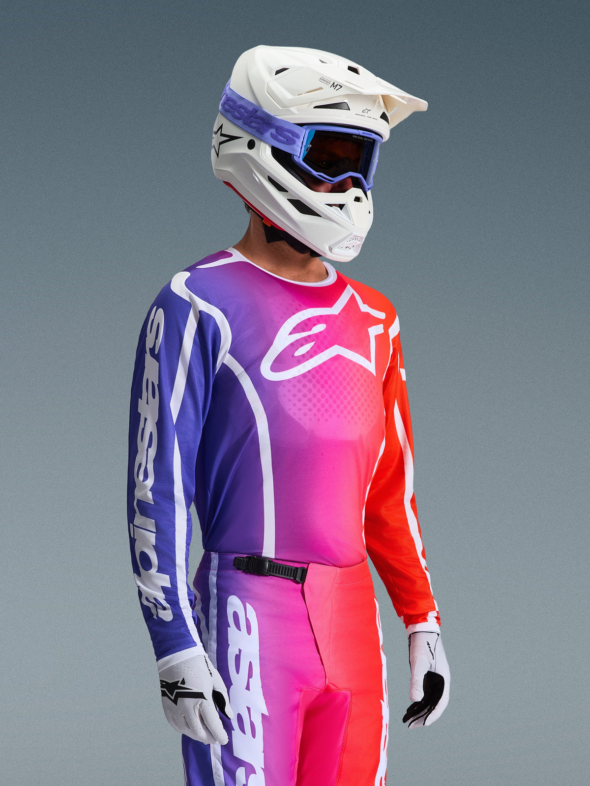 Alpinestars 2026 Fluid Apex Trikot, Motocross-Trikot, lebendiger Farbverlauf in Lila, Pink und Orange, kombiniert mit passender Hose, weißem Helm mit blauer Goggle und weißen Handschuhen, sportliches Design für Offroad-Performance und Mobilität