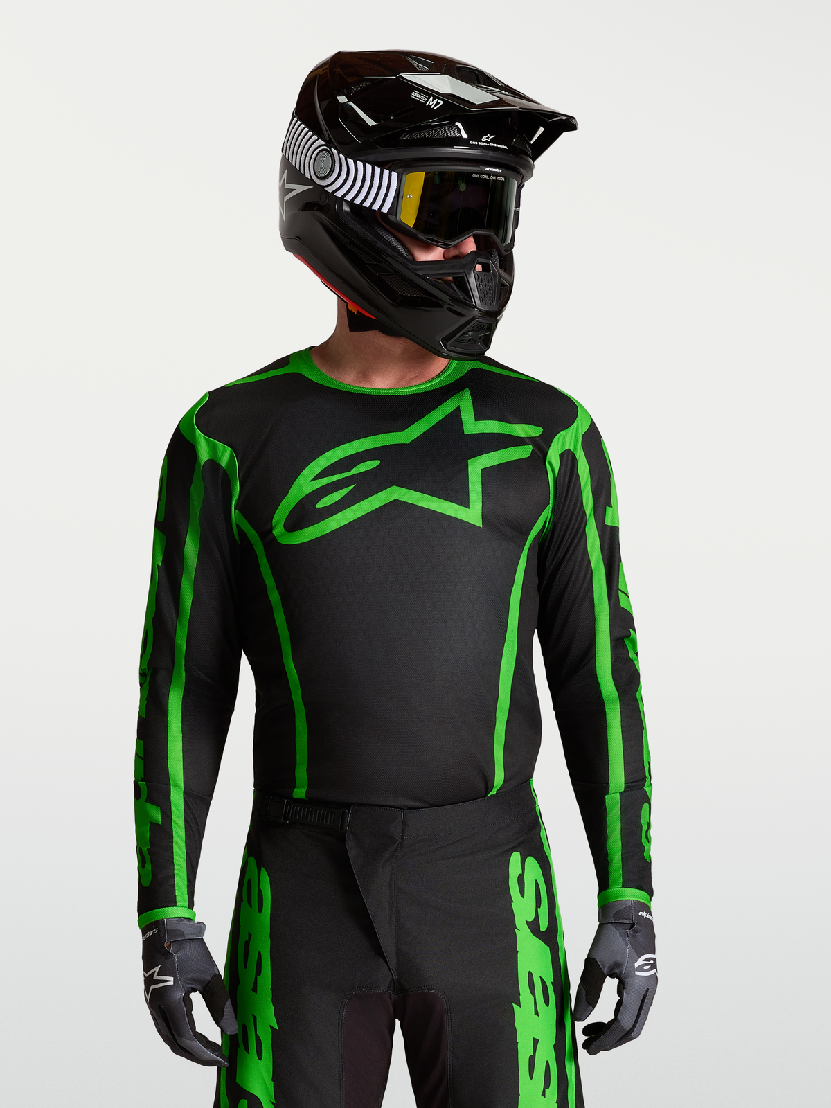 Alpinestars Fluid Apex V2 Trikot, Motocross-Oberteil in Schwarz und Fluo-Grün, getragen von Model mit Helm und Handschuhen.