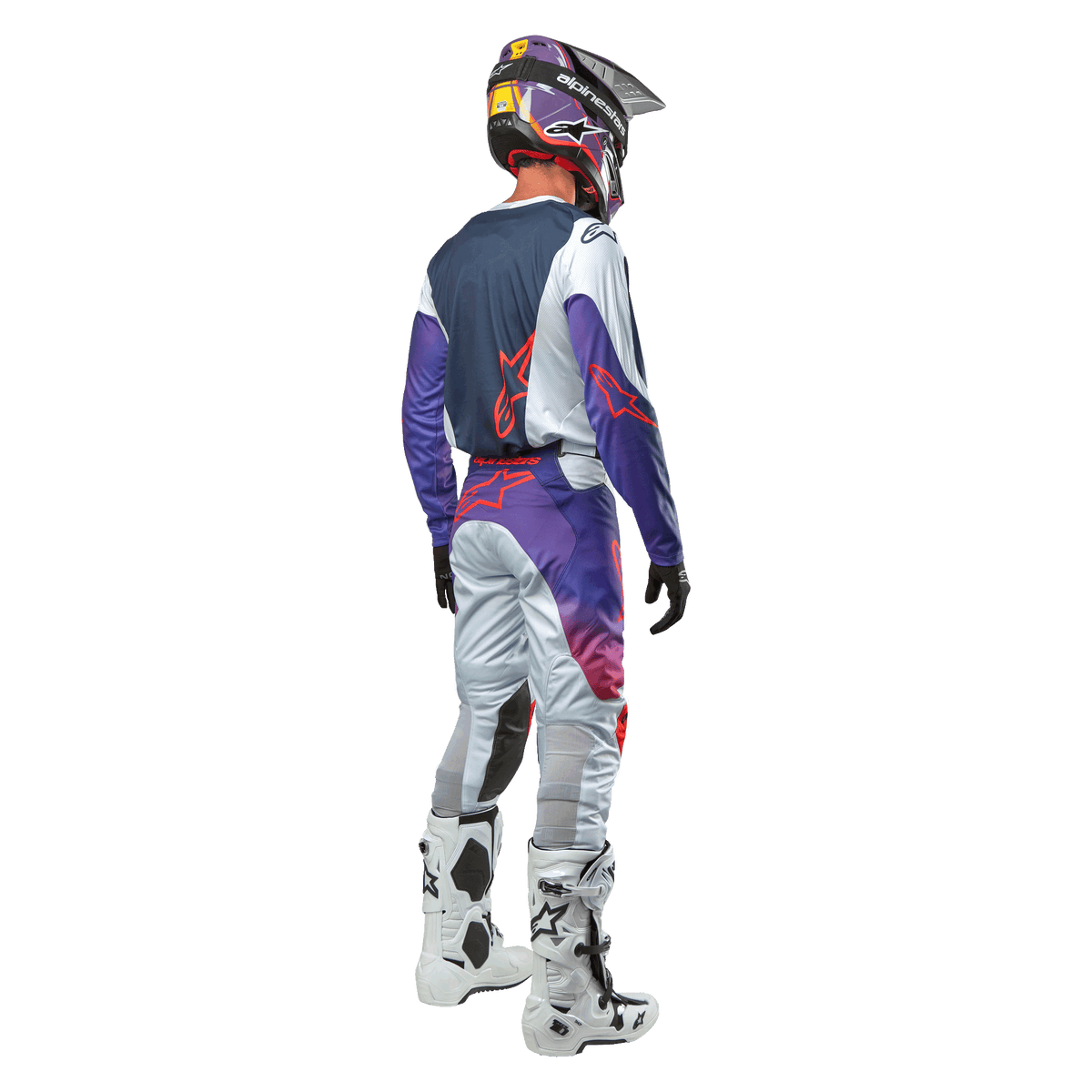 Motocross rider seen from behind wearing the Alpinestars 2024 Racer Hoen Jersey in Light Gray Hot Orange Black, navy back panel with orange star logo, purple sleeves, worn with matching racing pants and white boots.