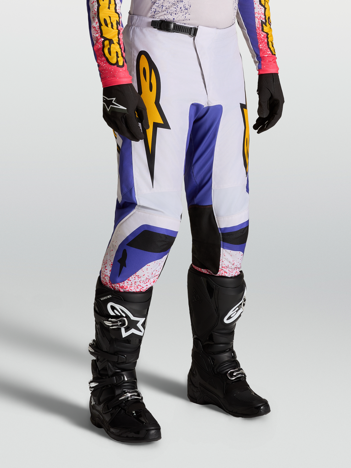 Alpinestars Fluid Drag Hose, Motocross-Hose f1r Herren, Blau und Flieder mit Gold-Grafiken, ergonomisches Sport-Fit-Design, getragen mit schwarzen Stiefeln.