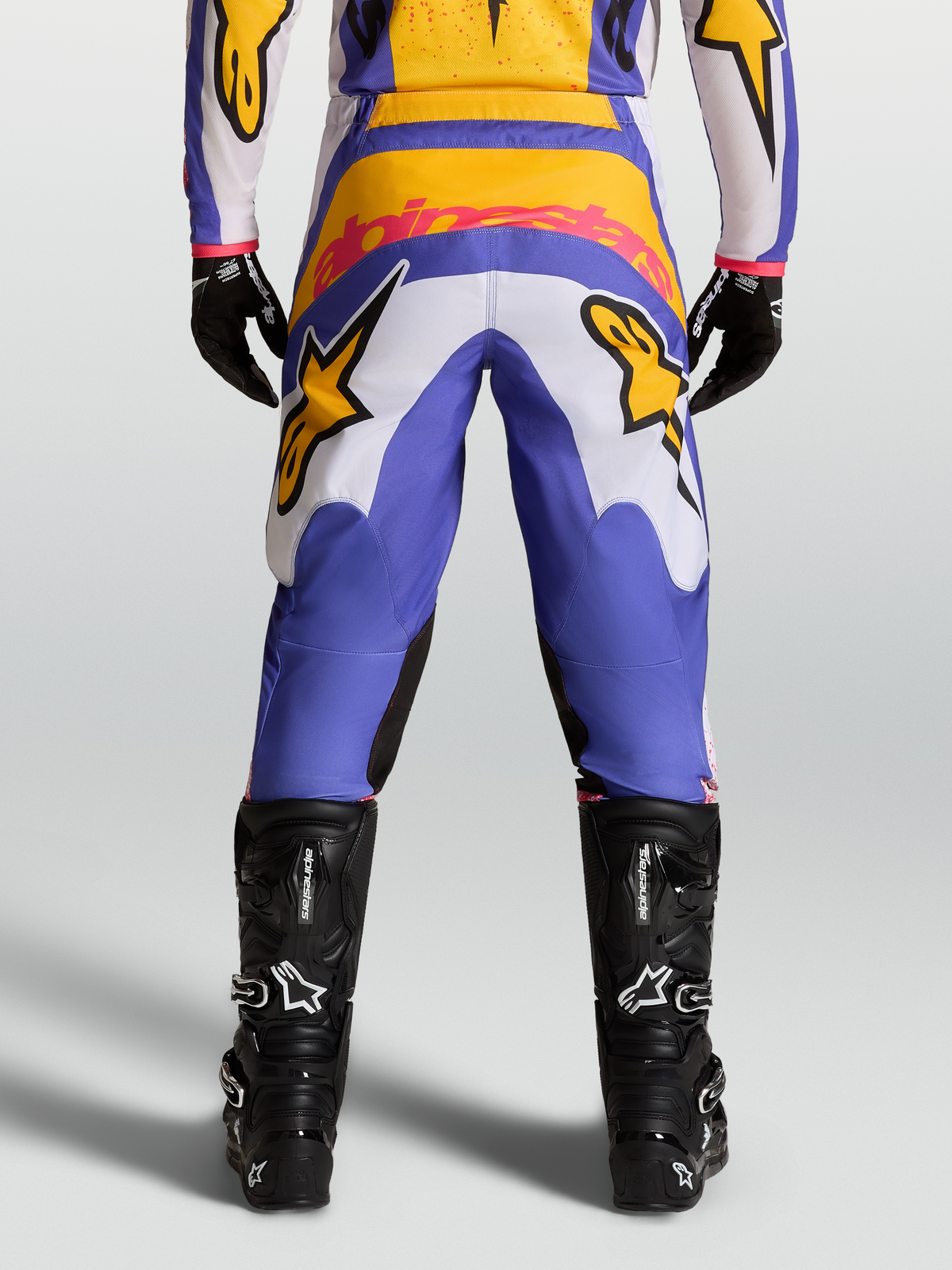 Alpinestars Fluid Drag Hose, Motocross-Hose in Blau und Gold, Rückansicht mit verstärktem Sitz, Stretch-Cord-Einsätzen und schwarzen technischen Stiefeln.