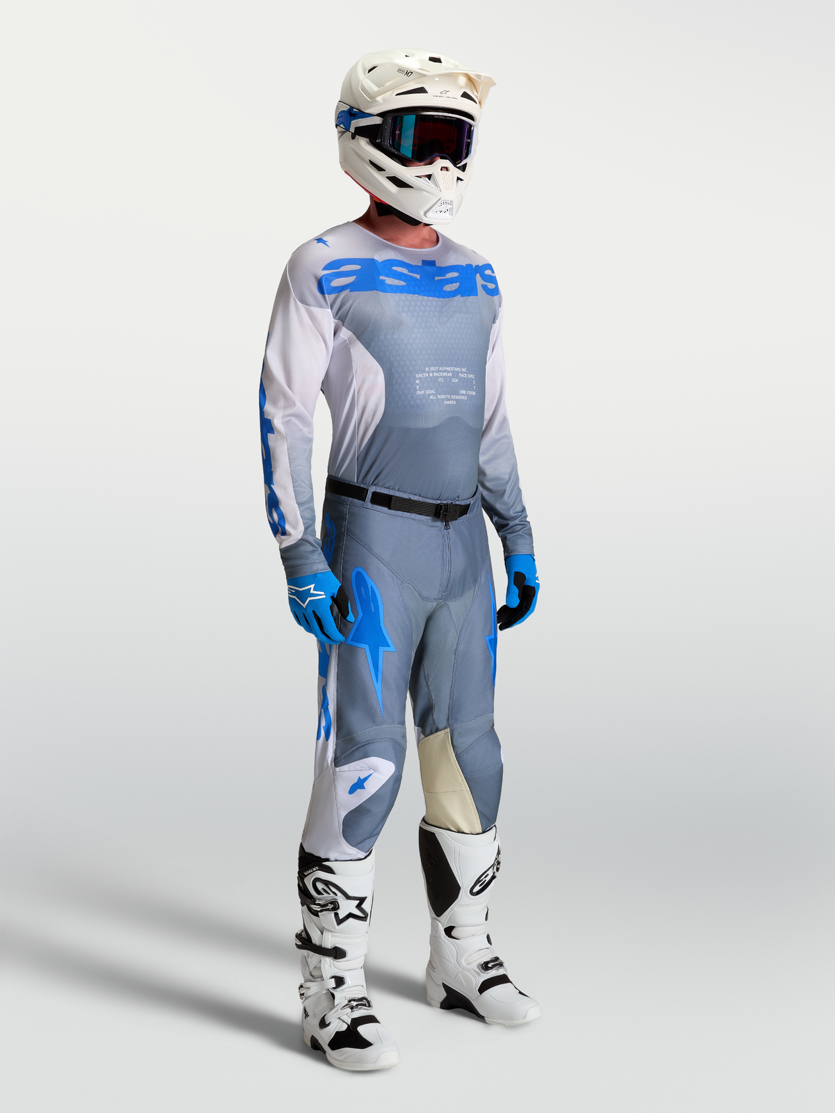Alpinestars Racer Amber Trikot, aschgraue und UCLA-blaue Motocross-Ausrüstung für Herren am Model mit Helm und Stiefeln.