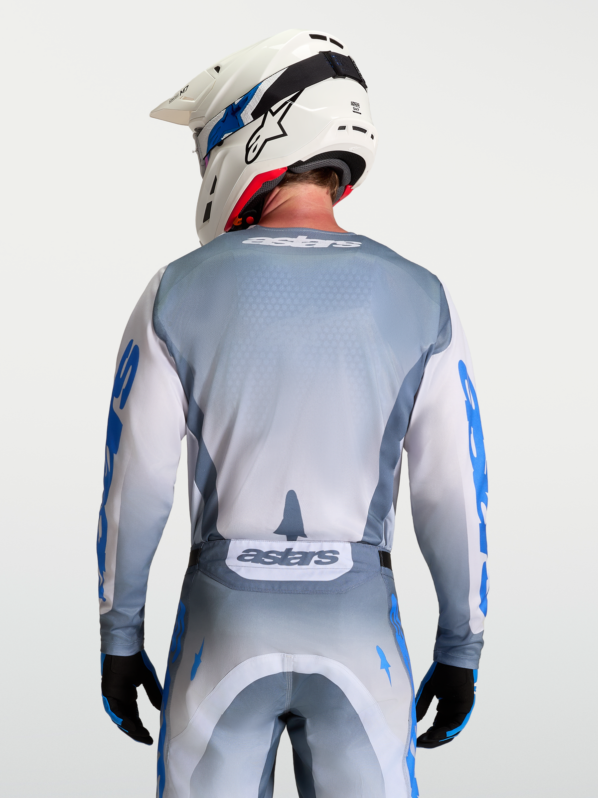 Alpinestars Racer Amber Trikot, Motocross-Trikot in Aschgrau und Weiß, rückseitige Modellansicht mit weißem Helm, ergonomische Passform für Offroad-Rennen