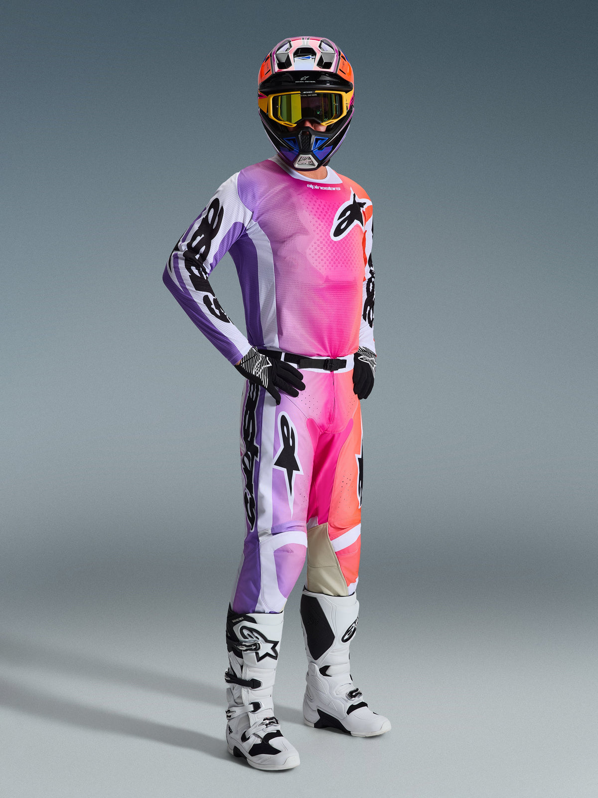 Alpinestars 2026 Racer Air Portl Gear Set, Motocross rider in full racing gear, jersey and pants featuring a vibrant purple, pink, and orange gradient with black Alpinestars logos, white and black accents, coordinated multi-colored helmet with yellow-tinted goggles, white and black motocross boots, black and white gloves.