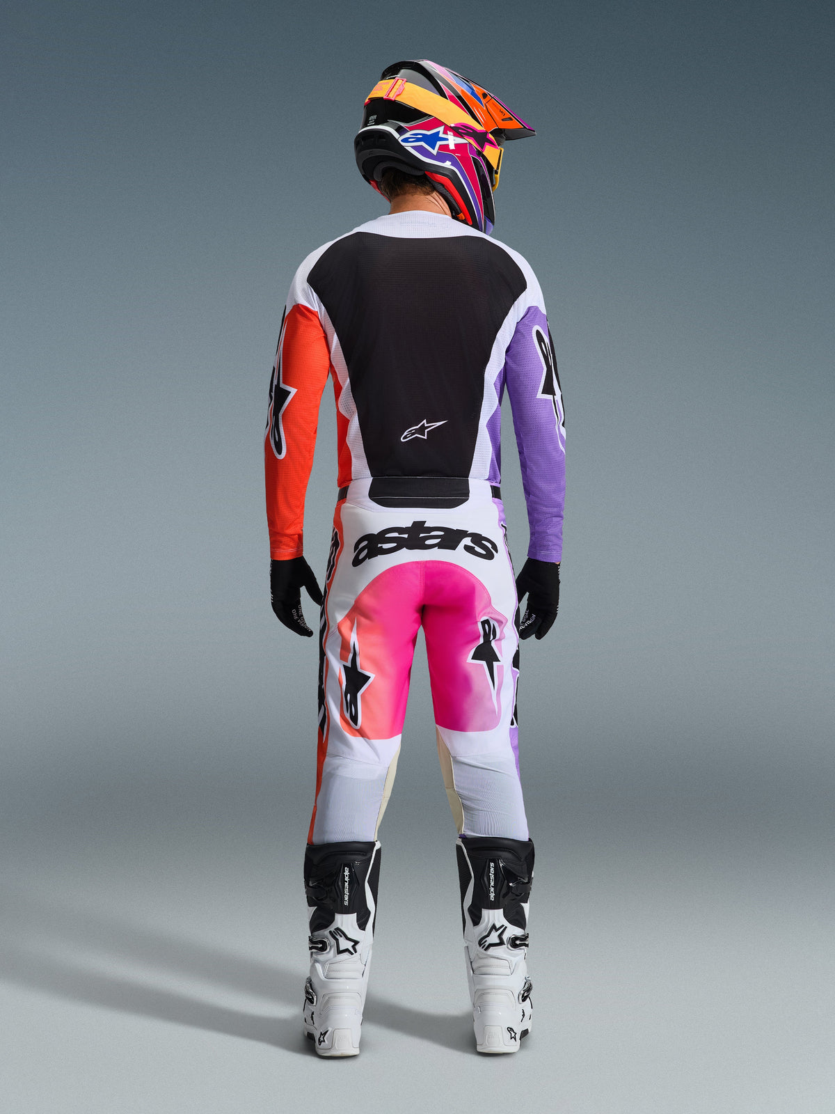 Alpinestars 2026 Racer Air Portl Gear Set, rear view of motocross rider wearing jersey with black back and orange and purple sleeves, white pants with pink and orange gradient and bold 'astars' branding, coordinated multi-colored helmet and white boots, professional off-road racing kit