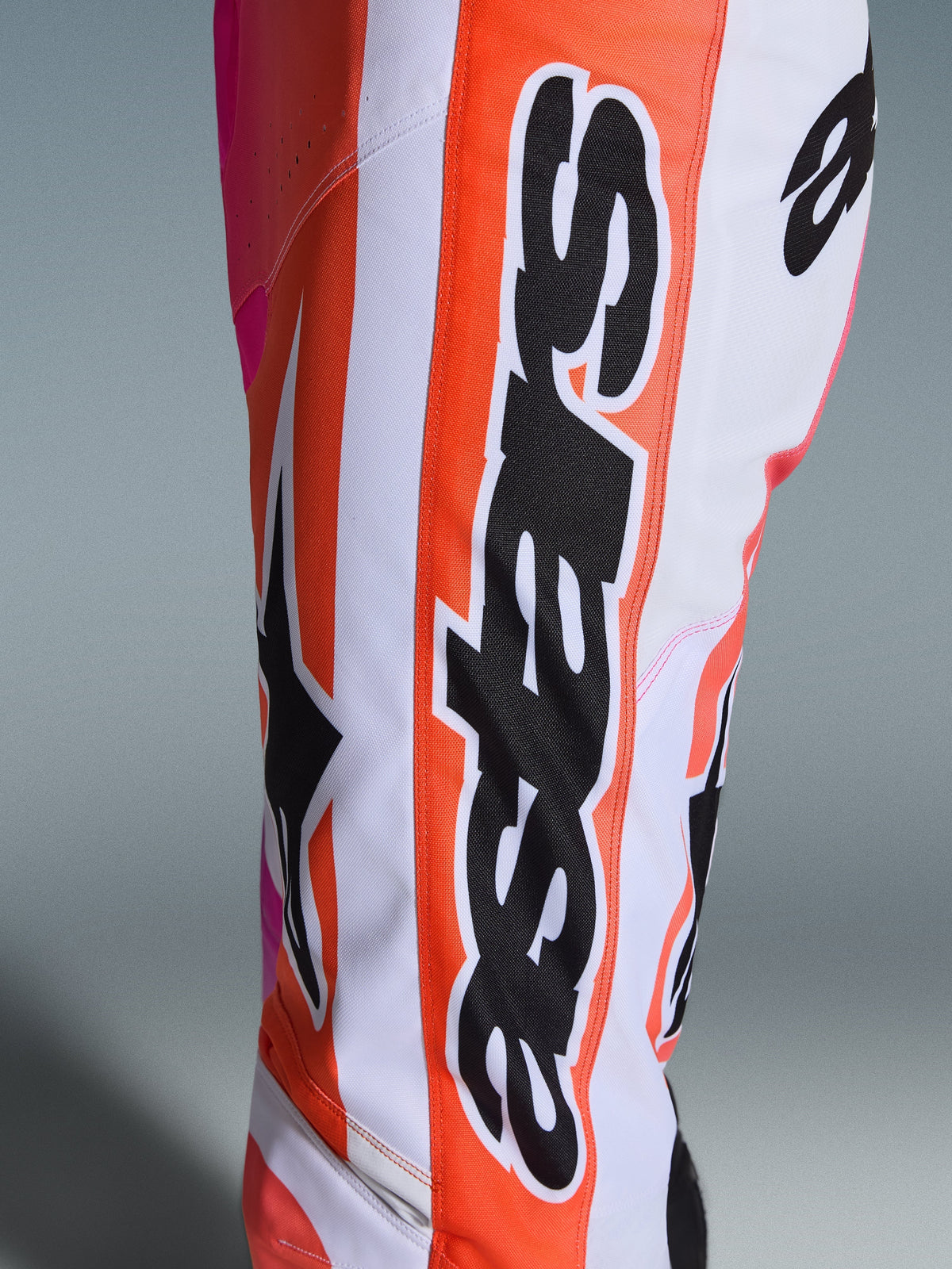 Alpinestars 2026 Racer Air Portl Pants, Motocross Pants, White Orange and Pink, close-up of leg featuring vertical black Alpinestars branding on an orange stripe, large black Astars logo, and breathable perforated fabric.