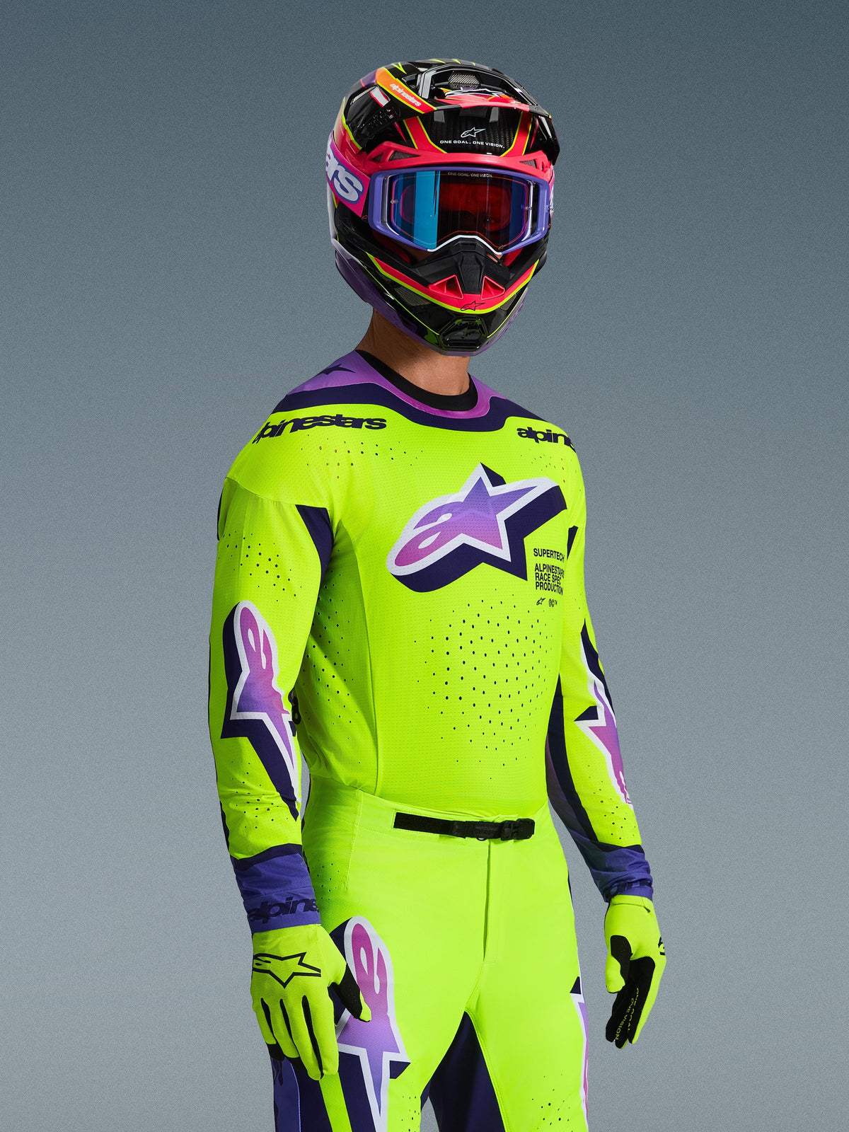 Motocross rider wearing the Alpinestars 2026 Supertech Vista Jersey, Bright Yellow with Purple and Black accents, matching yellow pants and gloves, multi-colored helmet with purple goggles, featuring laser-cut perforations and a large Astar logo on the chest, coordinated pro-level racing outfit