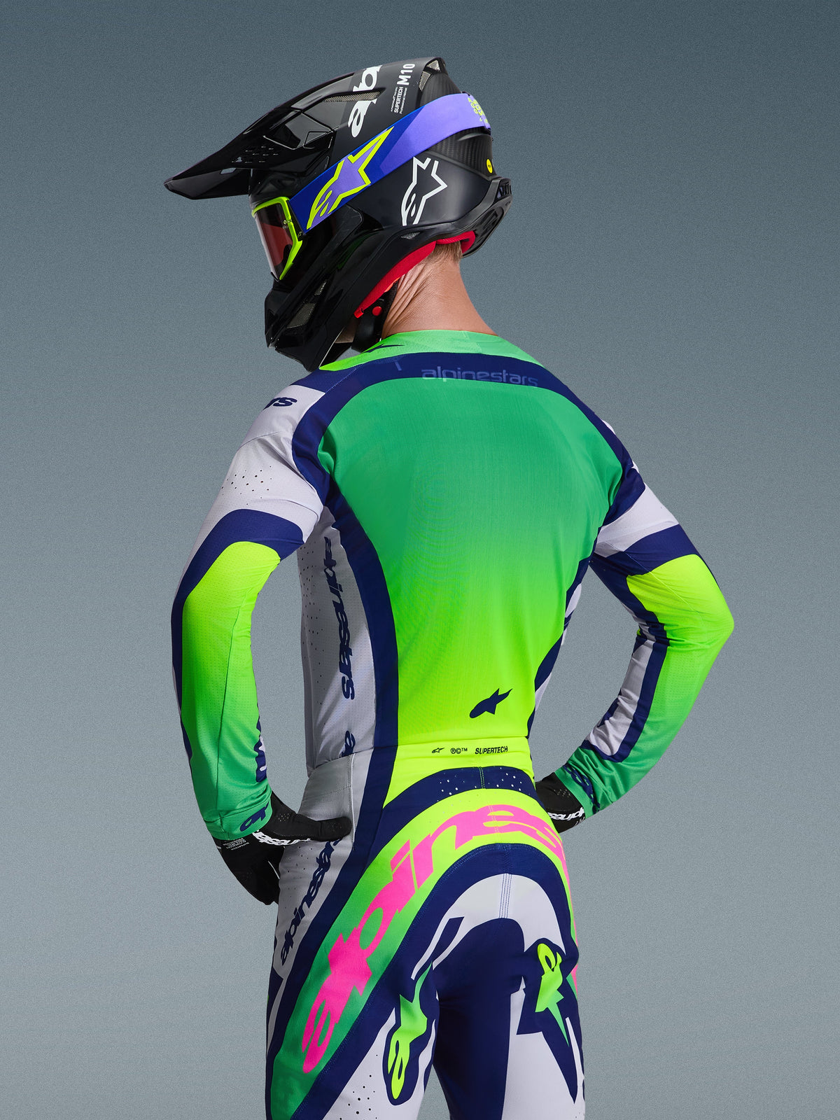 Motocross rider from the back wearing the Alpinestars 2026 Supertech Vista Jersey in Light Gray Yellow Fluo Blue, paired with matching motocross pants and helmet, featuring vibrant neon panels and athletic race fit for off-road racing.