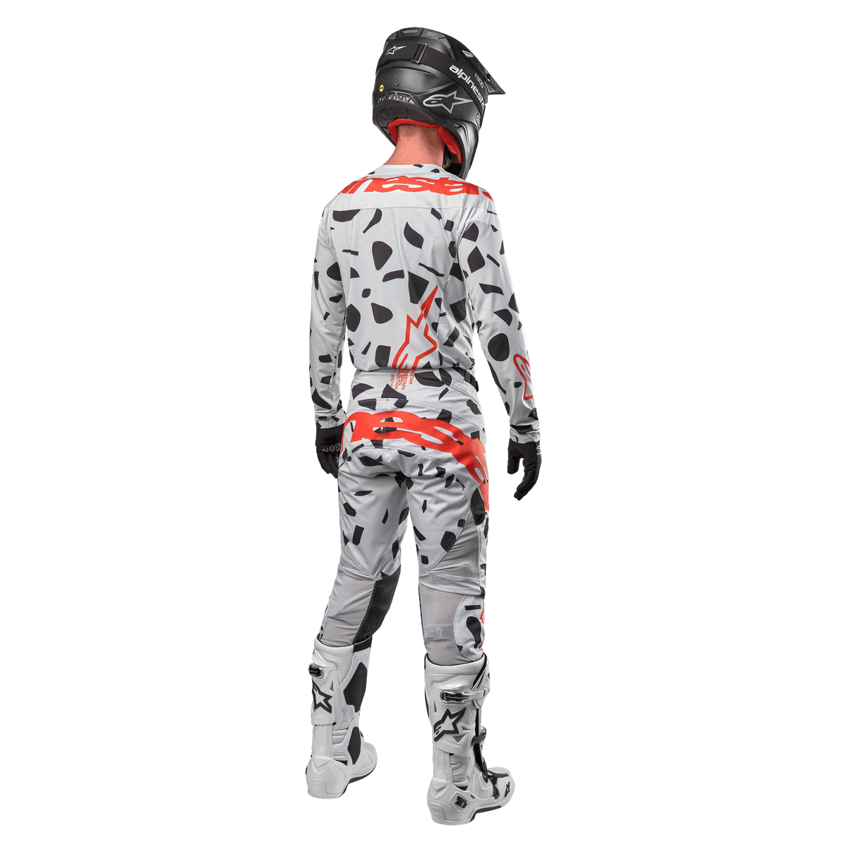 Motocross-Fahrer von hinten mit Alpinestars 2024 Techstar Rantera Trikot und passender Hose, Haze Gray Camo-Muster mit markanten roten Alpinestars-Logos, schwarzer Helm, weiß-schwarze Stiefel, schwarze Handschuhe, koordiniertes Motocross-Ausrüstungsset.