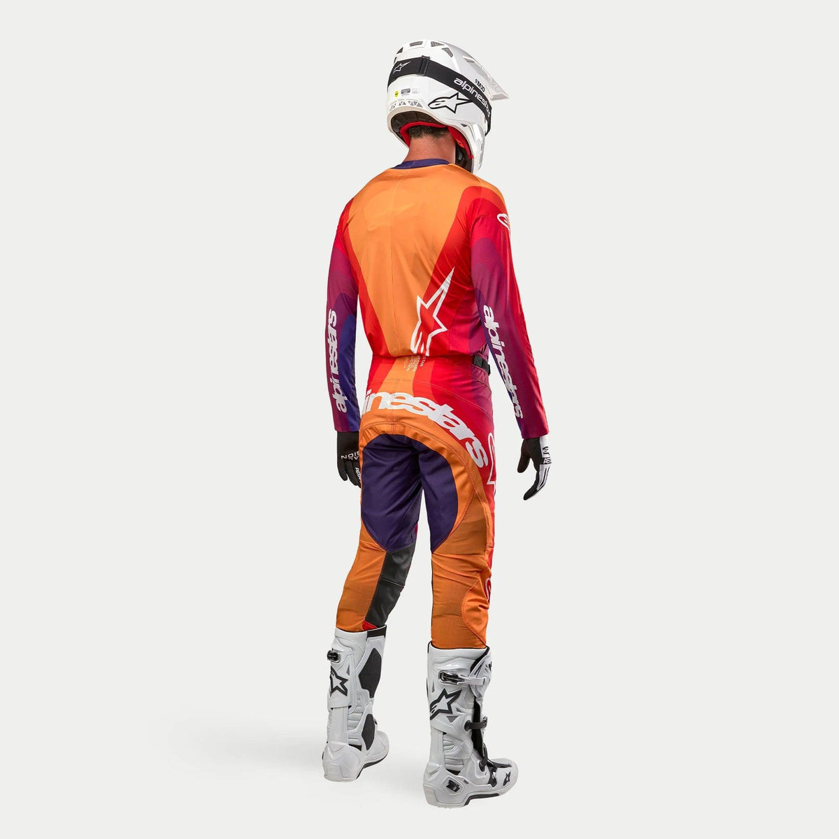 Alpinestars 2024 Techstar Pneuma Ausrüstung, Motocross-Komplettset in Dunkelviolett, Orange und Dunkelblau, Rückansicht des Fahrers mit passendem Helm, Trikot, Hose und weißen Stiefeln, professionelles Design für den Rennsport.