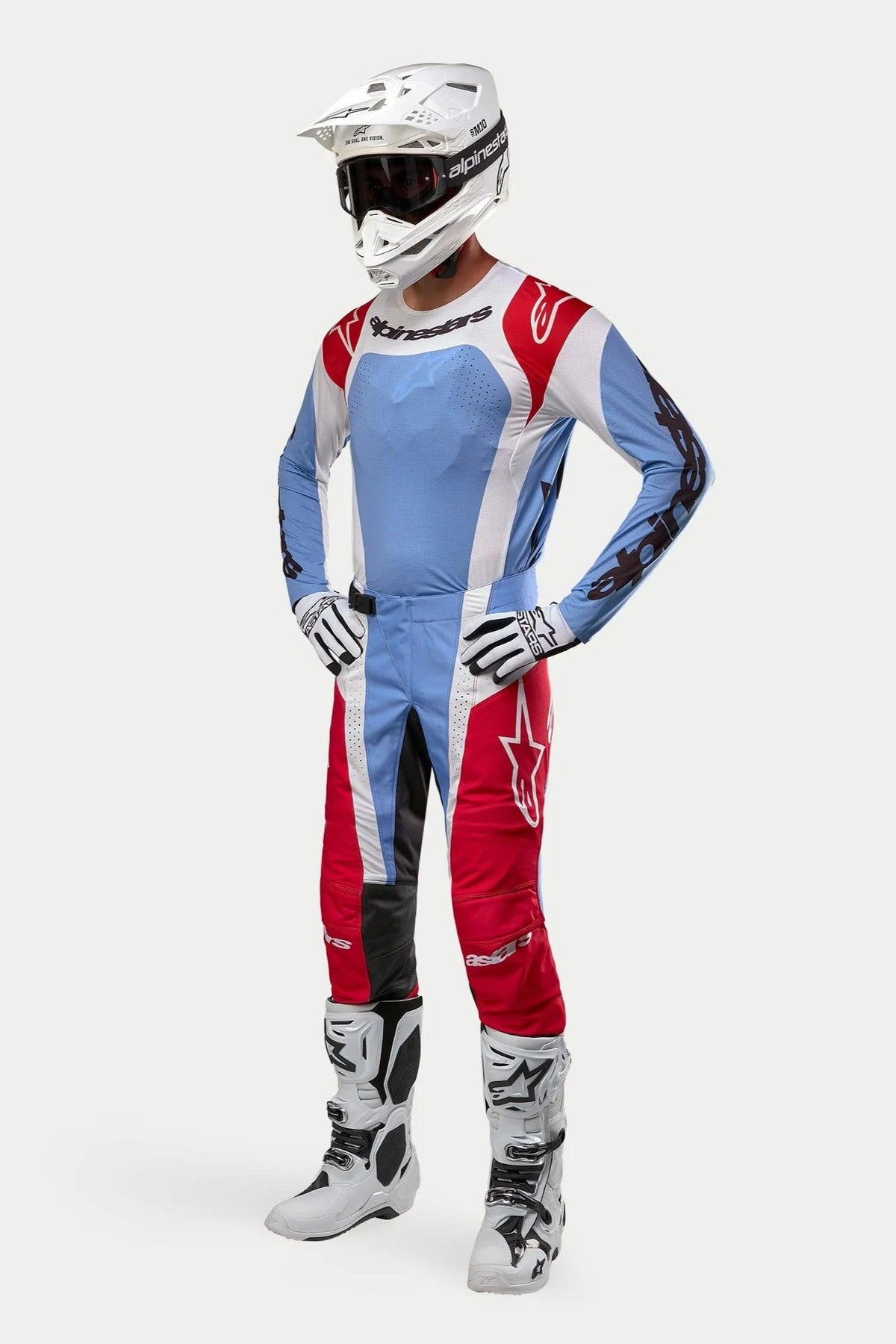 Motocross-Fahrer in kompletter Rennausrüstung mit dem Alpinestars 2024 Techstar Ocuri Trikot in Hellblau, Marsrot und Weiß, passender Hose, weißem Helm mit Schutzbrille, weißen Stiefeln und weiß-schwarzen Handschuhen.