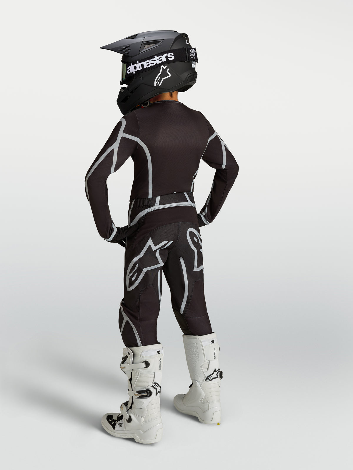 Alpinestars 2027 Jugend Fluid Apex V2 Motocross-Ausrüstungsset in Schwarz und Silber, Rückansicht mit weißen Stiefeln.