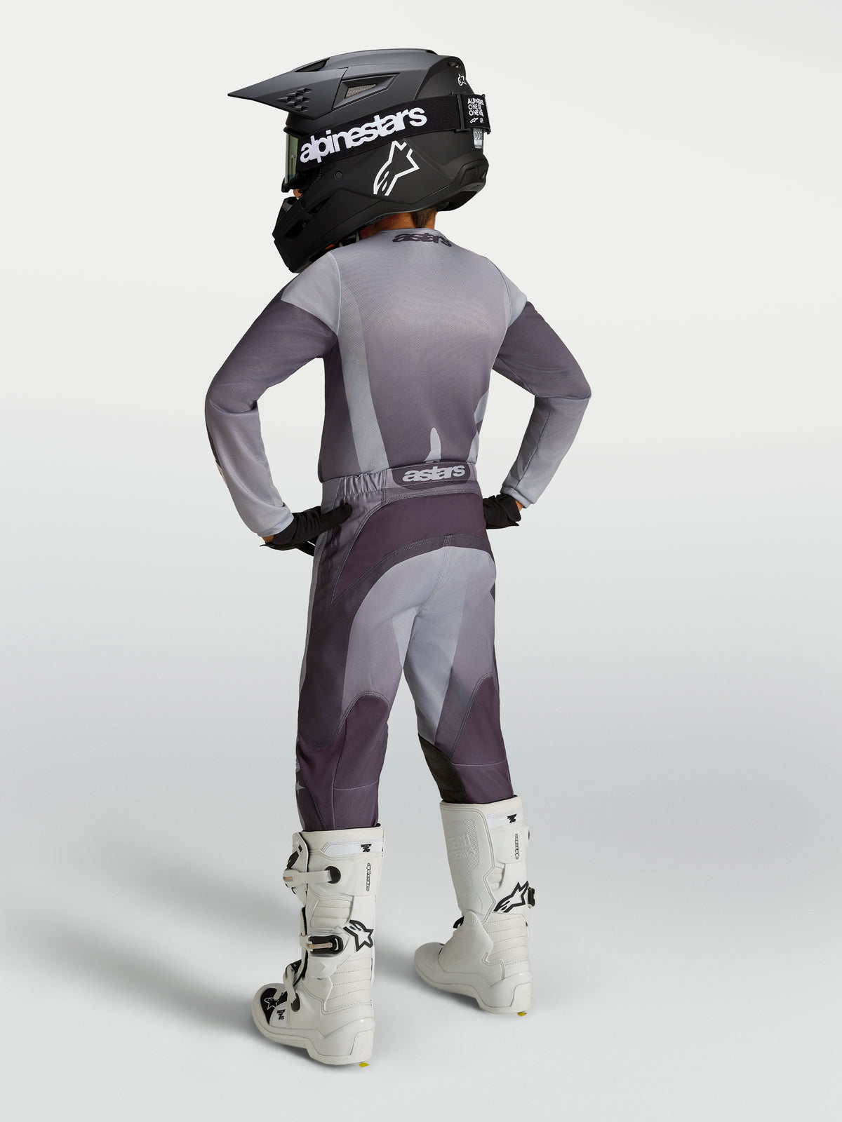 Alpinestars 2027 Jugend Fluid Amber Gear Set, Motocross-Outfit in Grau und Lila, Rückansicht mit Helm und weißen Stiefeln.