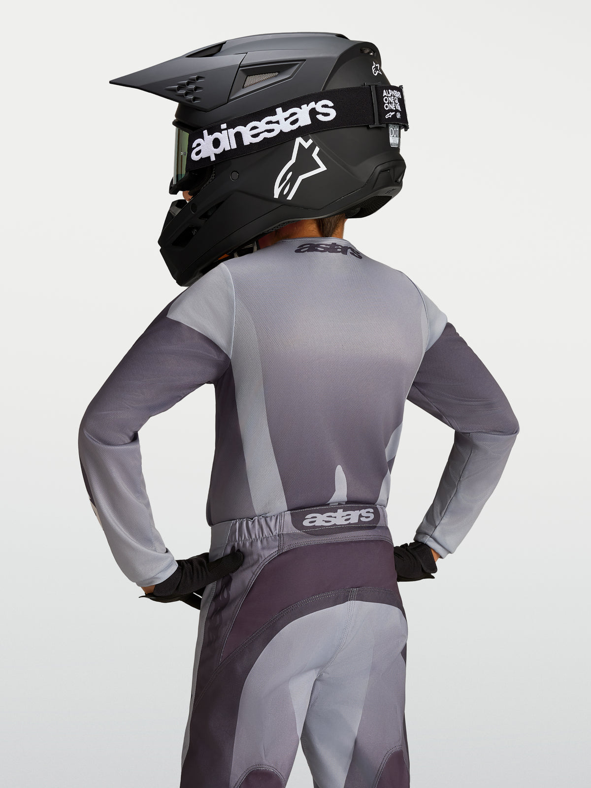 Alpinestars Fluid Jugend-Trikot Amber, Motocross-Trikot in Grau und Sand, Rückansicht eines jungen Fahrers mit Helm.