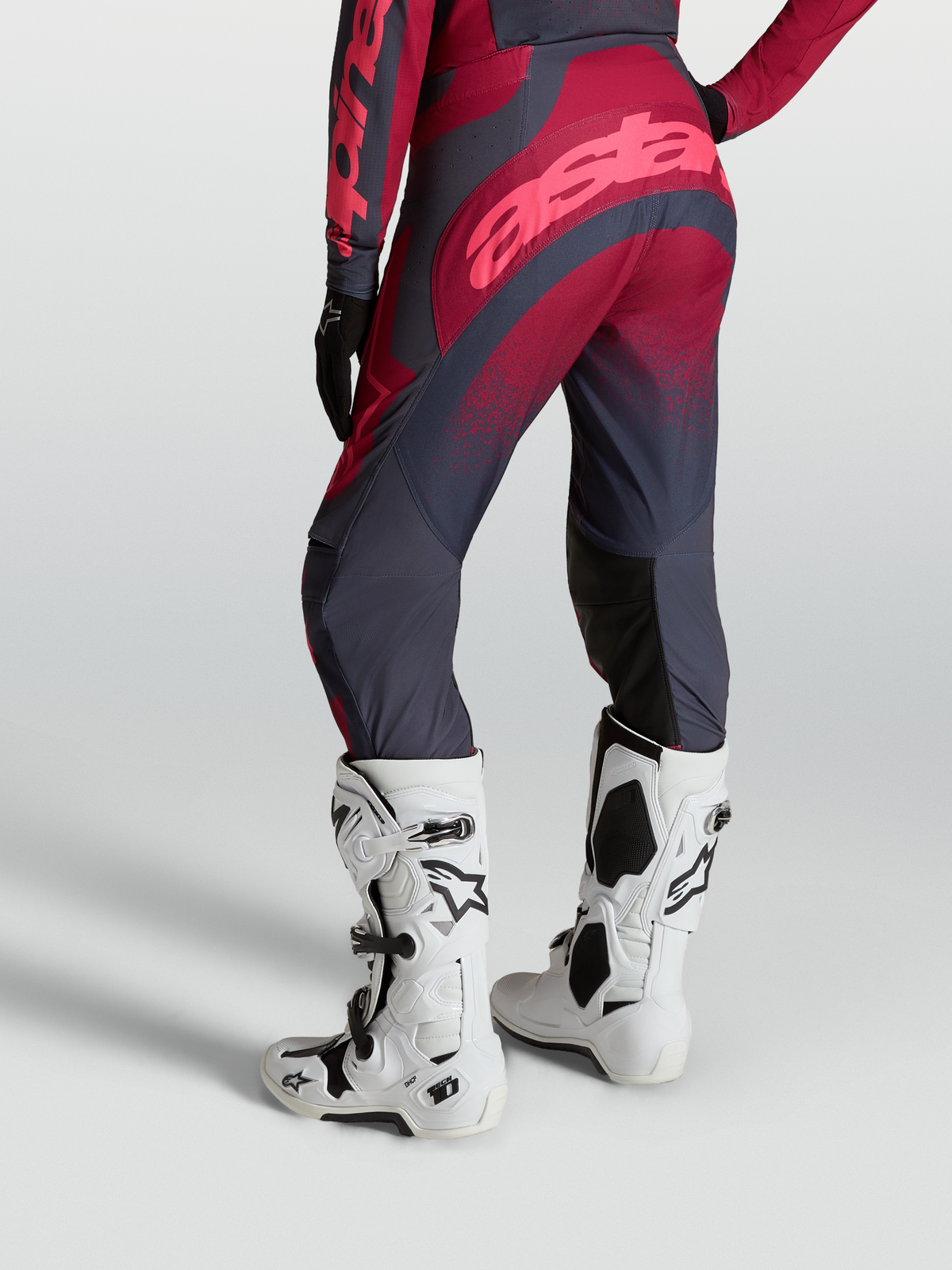 Alpinestars Stella Techstar Swan Hose von hinten, Crimson und Dunkelgrau, mit weißen Tech 10 Motocross-Stiefeln.