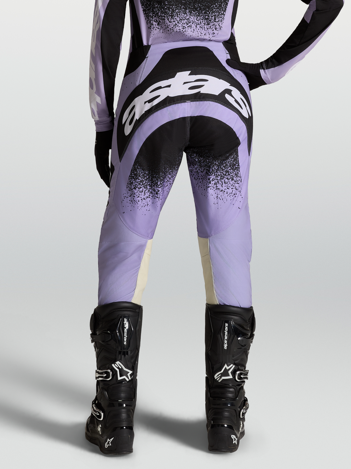 Alpinestars Stella Techstar Hose Swan, Damen-Motocross-Ausrüstung in Lila und Schwarz mit weißen Logos, getragen von einem Model mit schwarzen Stiefeln.