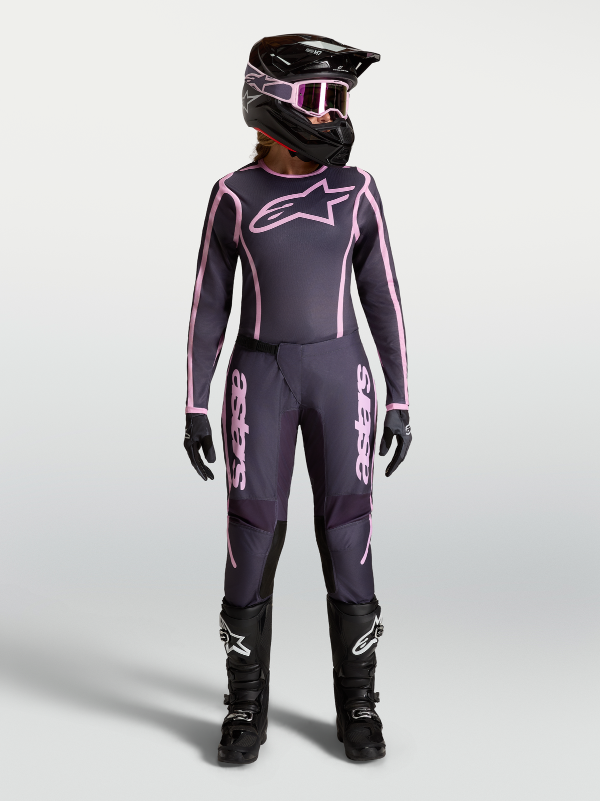 Alpinestars Stella Fluid Apex V2 Hose, Damen-Motocross-Hose, Grau und Pink, getragen von einem Model mit passendem Trikot, Helm und MX-Stiefeln, hochwertige Offroad-Schutzausrüstung.
