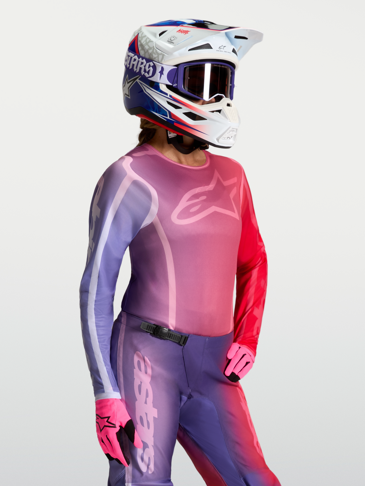 Alpinestars Stella Fluid Kepler Trikot, Damen-Motocross-Trikot in Lila und Rot, feuchtigkeitsableitendes Polygewebe, getragen von einem Model mit Helm und Handschuhen