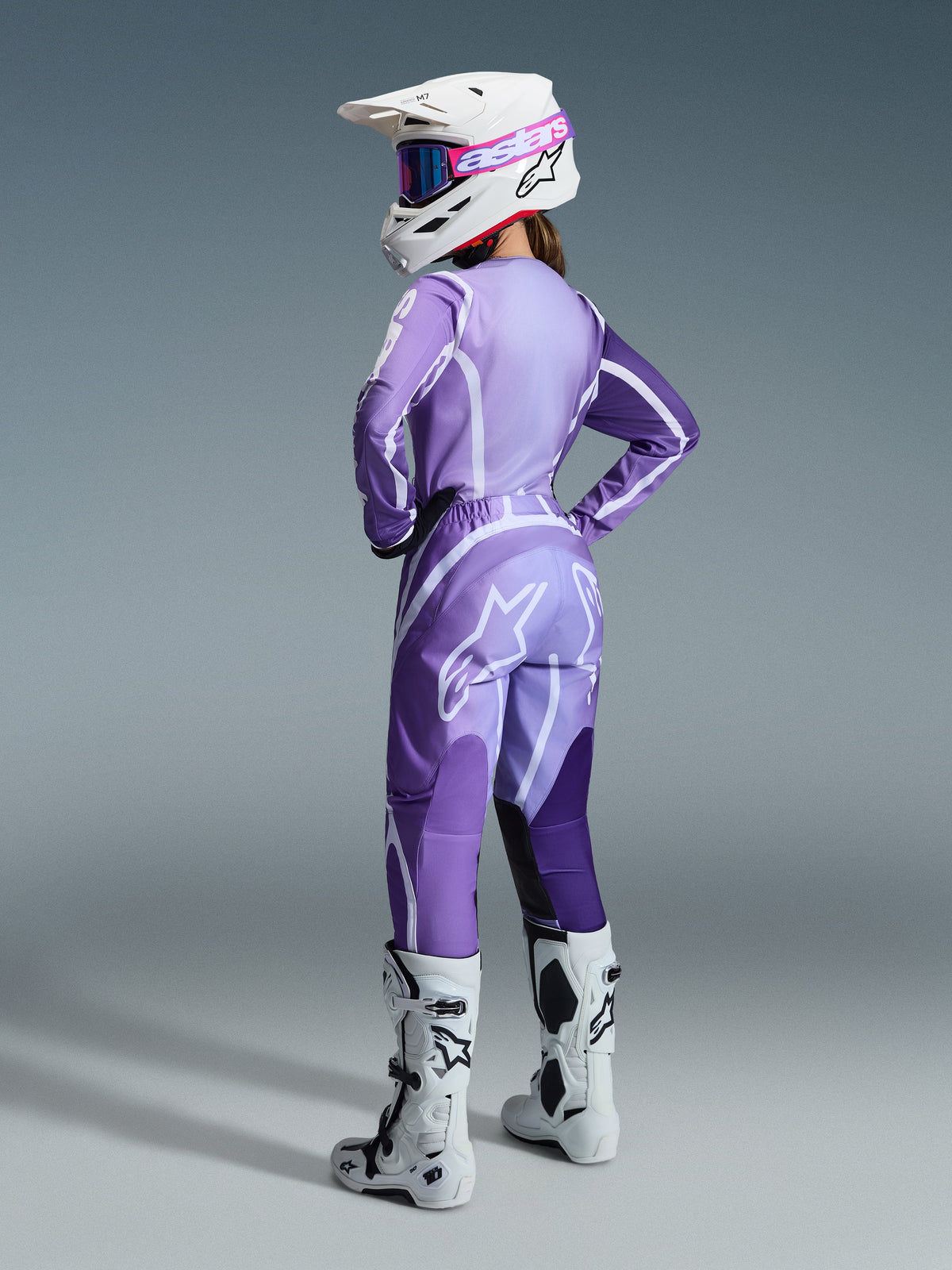 Motocross-Fahrerin im 2026 Stella Fluid Apex Bekleidungsset für Damen, lila- und lavendelfarbenes Trikot und Hose mit weißen Akzenten, weißer Helm mit rosa Brille, weiße und schwarze Stiefel, abgestimmtes Outfit für Offroad-Rennsport