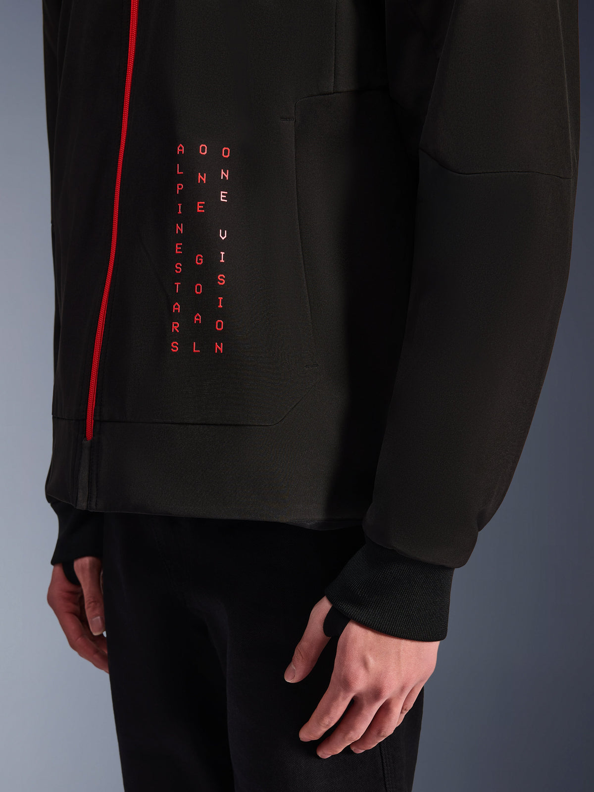 Alpinestars Radium Tech Hoodie, Urban Motorcycle Jacket, Black and Bright Red, close-up of front graphic with vertical red text "ALPINESTARS ONE GOAL ONE VISION", red zipper, and ribbed cuff with thumbhole.