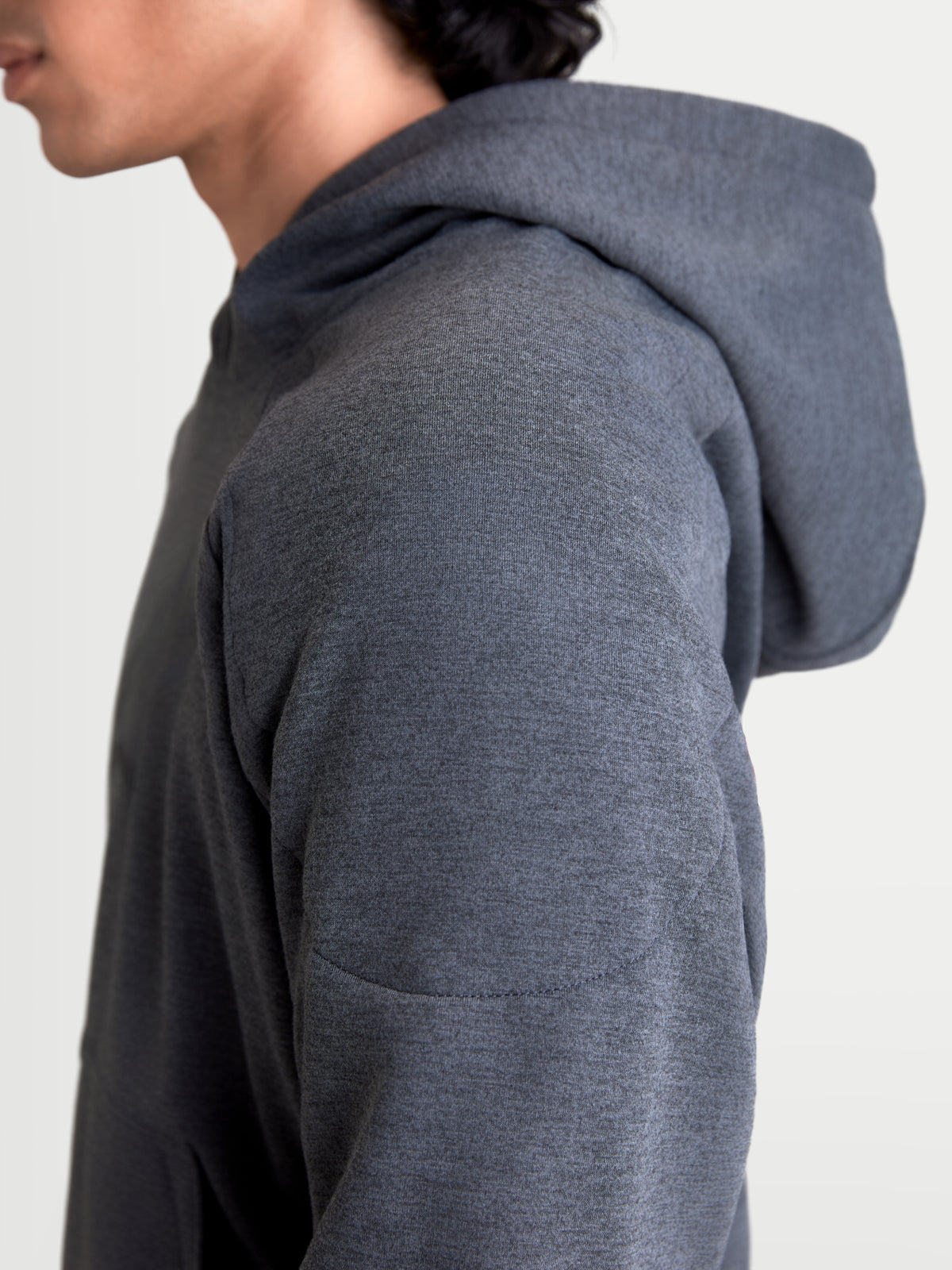 Alpinestars Ageless Kapuzenpullover, urbaner Herren-Motorradhoodie in Asphaltgrau meliert, Nahaufnahme des Seitenprofils mit gestrickter Materialkonstruktion und Schulterverstärkung am Model