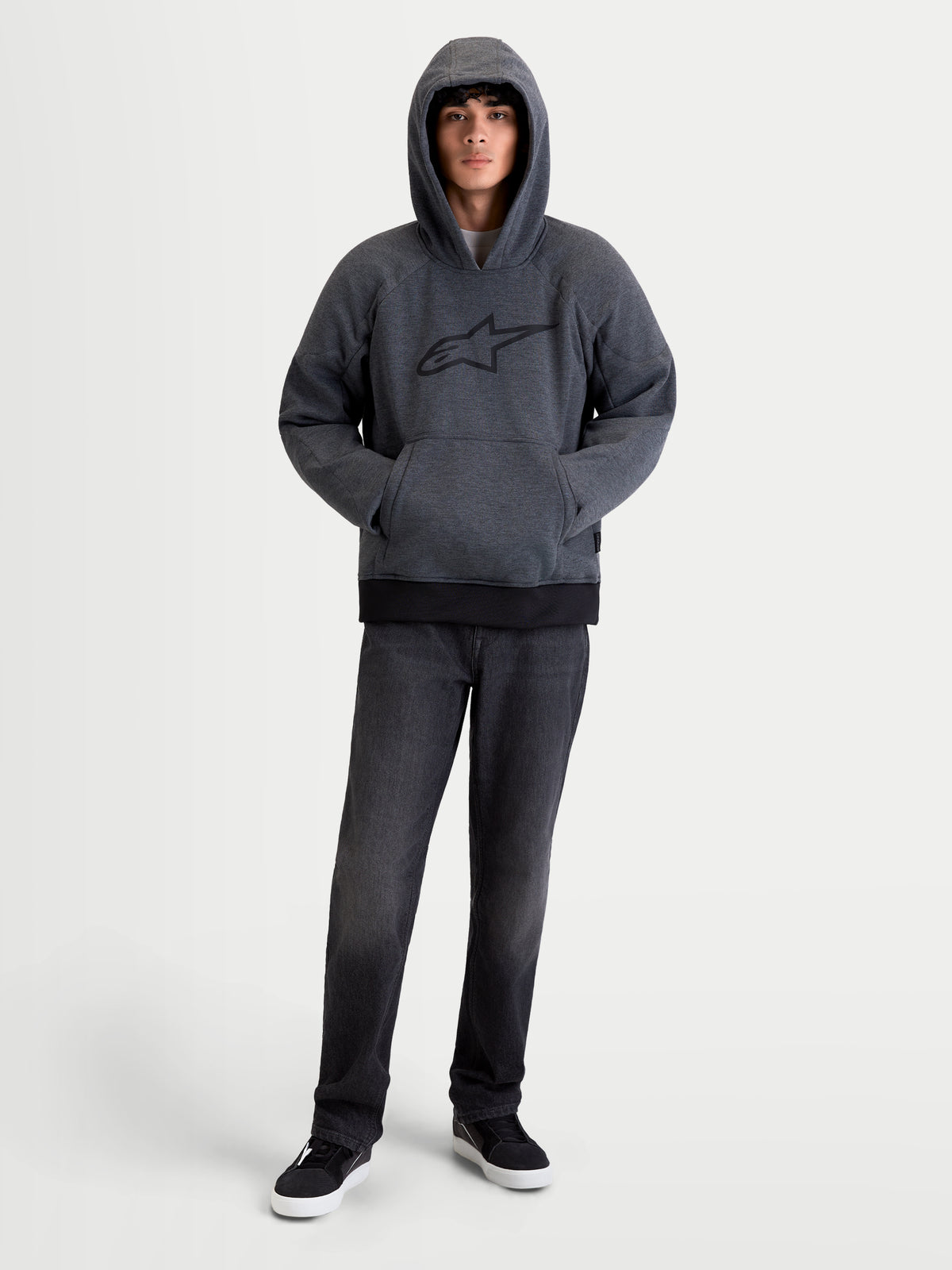Alpinestars Ageless Kapuzenpullover, urbaner Motorrad-Kapuzenpullover für Herren in Asphalt Melange Grau, Vorderansicht an einem Model mit hochgezogener Kapuze, mit integrierten Nucleon-Schulter- und Ellbogenprotektoren sowie Kängurutasche vorne