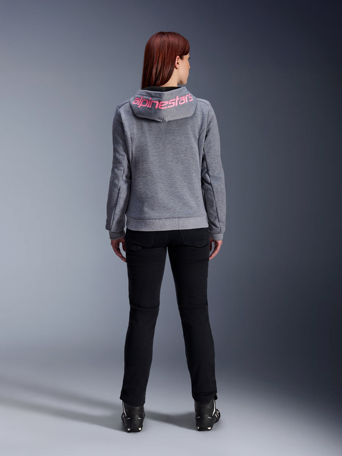 Alpinestars Stella Chrome V2 Sport Hoodie, Motorrad-Kapuzenjacke für Damen, Grau Meliert und Pink Fluo, Rückansicht mit pinkem Alpinestars-Logo auf der Kapuze, getragen mit schwarzer Motorradhose und Stiefeln, lässige Motorradbekleidung für Damen