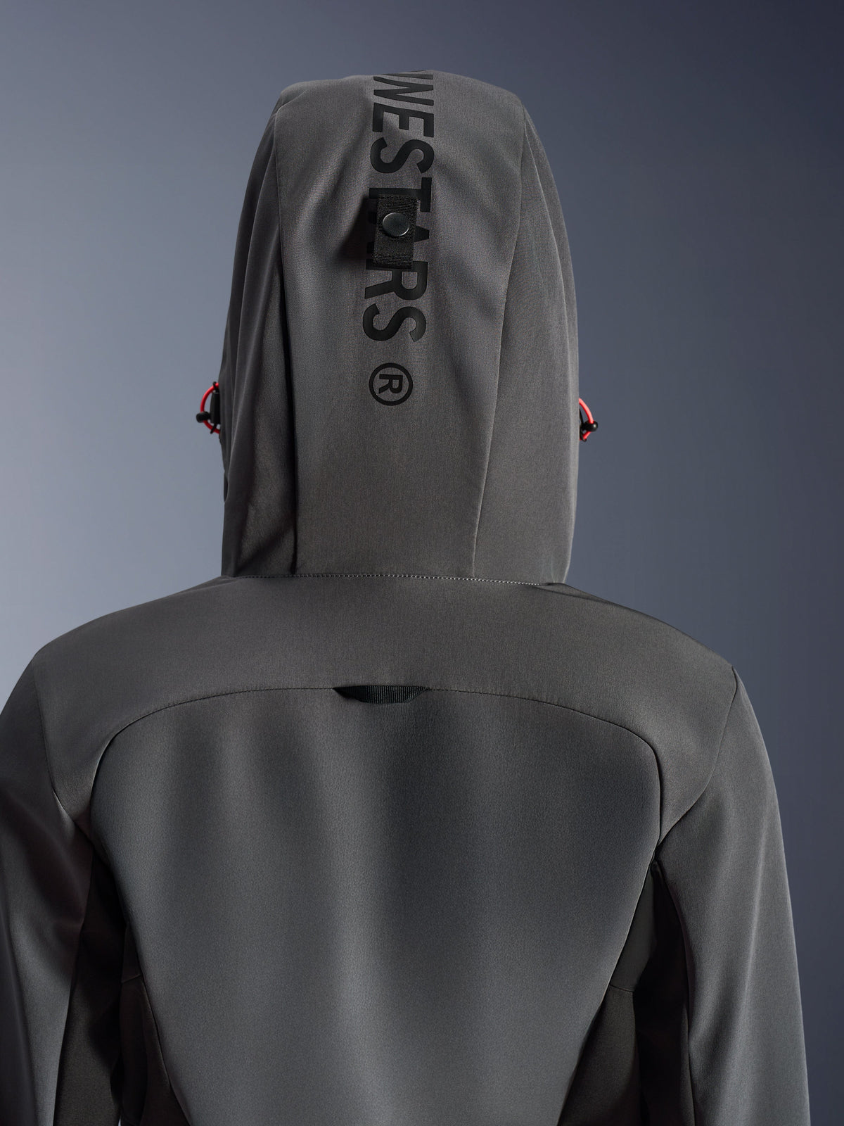 Alpinestars Stella Radium Tech Hoodie für Damen, Dunkelgrau Schwarz, Nahaufnahme der Rückansicht mit Kapuze, vertikaler Schriftzug und Befestigungsschlaufe, rote Kordelzug-Akzente, strapazierfähige winddichte 3-Lagen-Textilkonstruktion für urbanes Motorradfahren.
