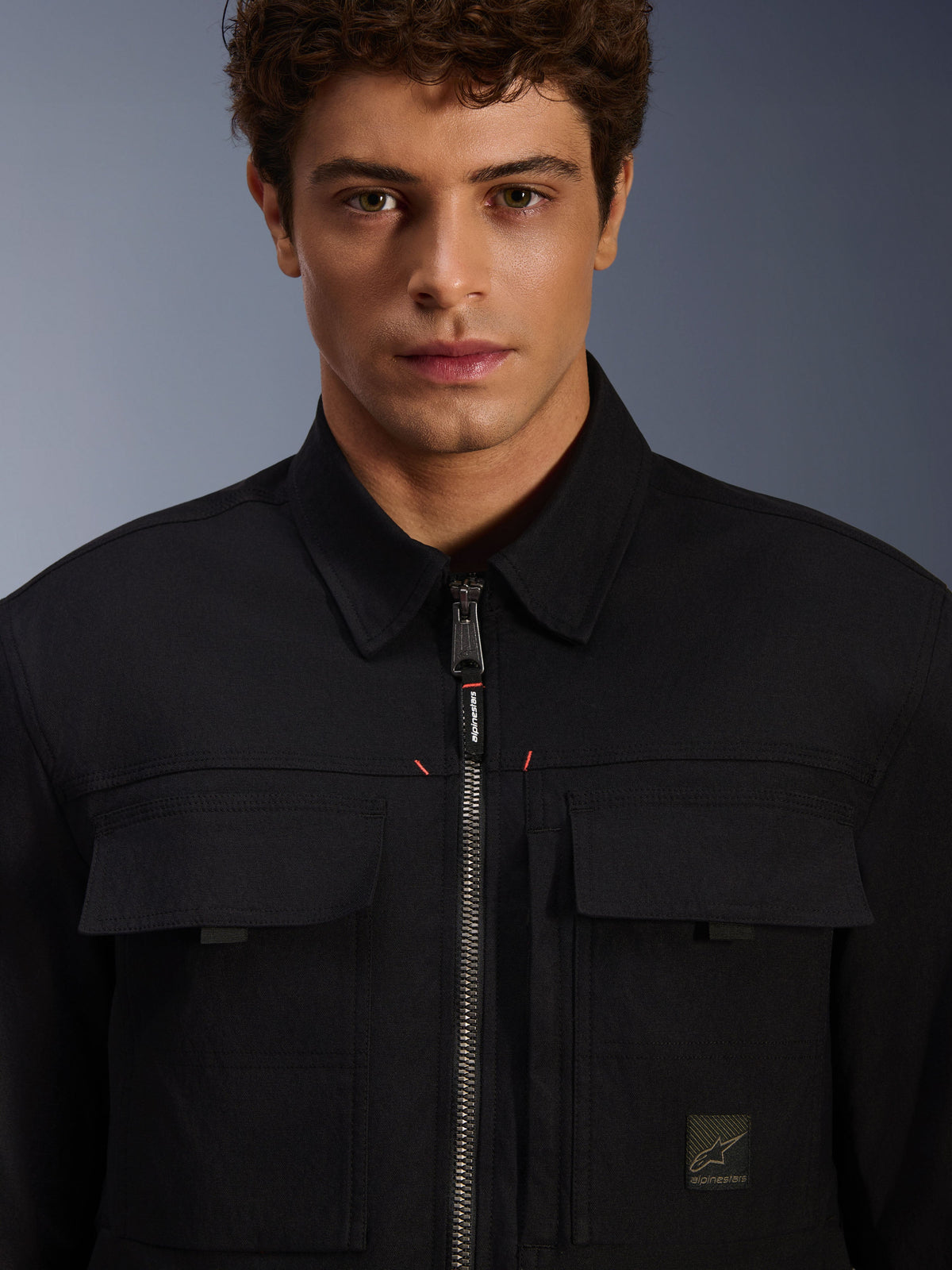 Alpinestars Bryon wasserabweisendes Überhemd, Schwarz, Detailansicht von Frontreißverschluss und Brusttaschen, strapazierfähige gewachste Canvas-Struktur, minimalistisches urbanes Design mit Marken-Akzenten und gewebtem Logo-Etikett
