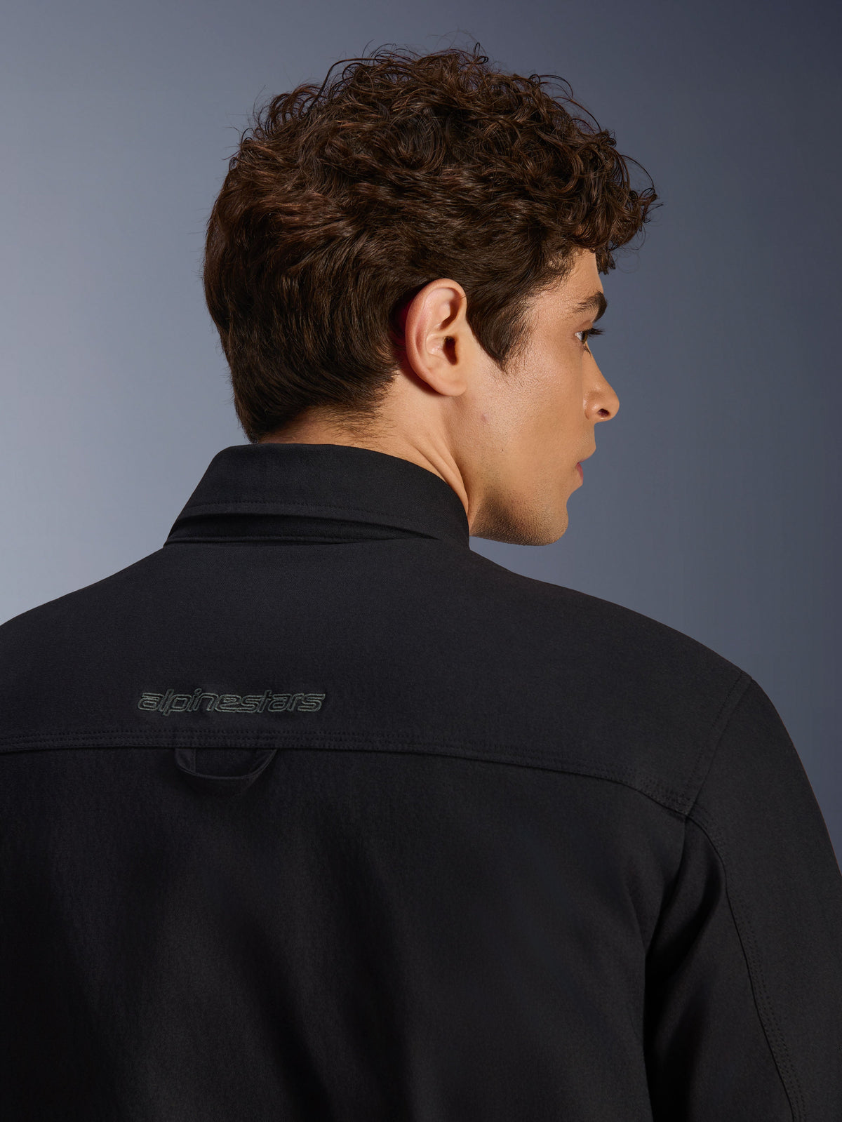Alpinestars Bryon Water Resistant Overshirt, urbane Motorradjacke, Schwarz, Nahaufnahme des hinteren Schulterbereichs mit besticktem Logo und Aufhängeschlaufe, wasserabweisende Konstruktion aus gewachstem Canvas