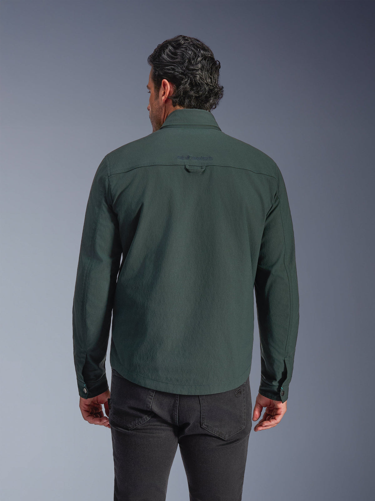Alpinestars Bryon wasserabweisendes Overshirt, Dark Emerald Grün, Rückansicht am Modell, besticktes Logo auf dem oberen Rücken, strapazierfähiger gewachster Canvas, urbane Motorradjacke kombiniert mit dunkler Hose