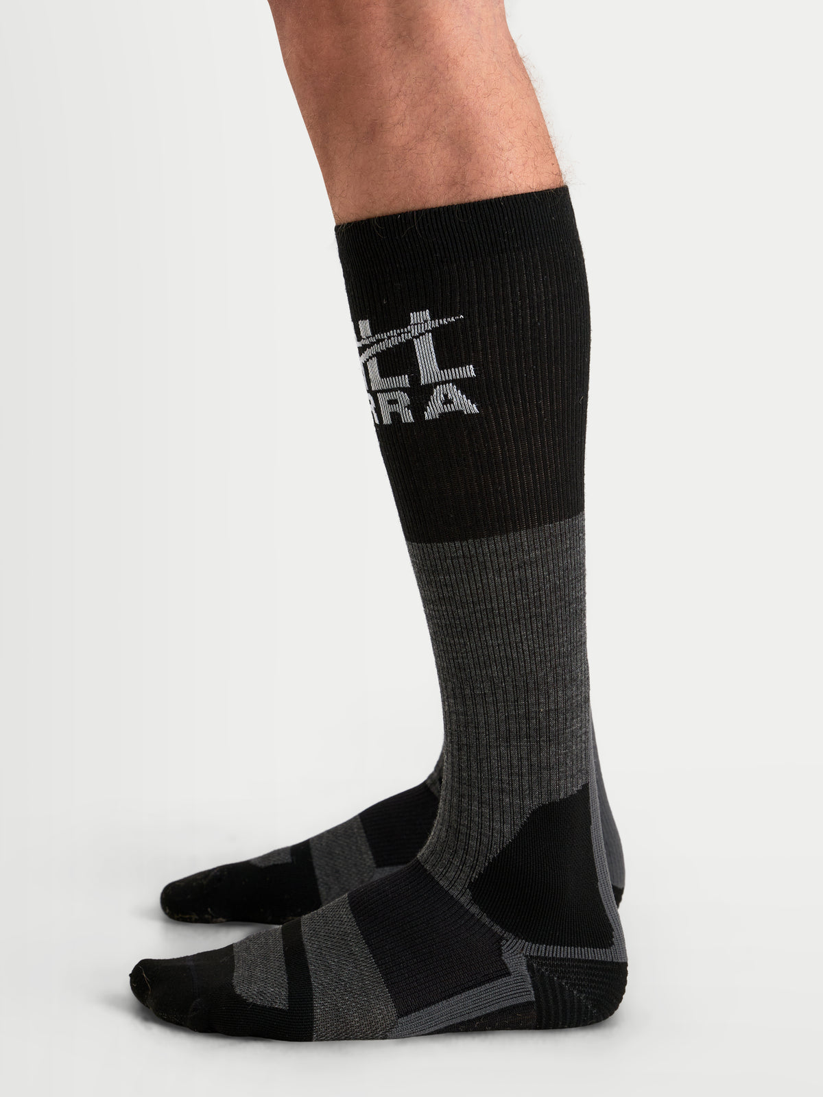 Alpinestars At 8 Merino Socken, Adventure-Motorradsocken in Tar-Grau und Schwarz, thermischer Merinowollmix mit geripptem Wadenbereich sowie verstärkter Ferse und Zehenpartie, getragen am Model