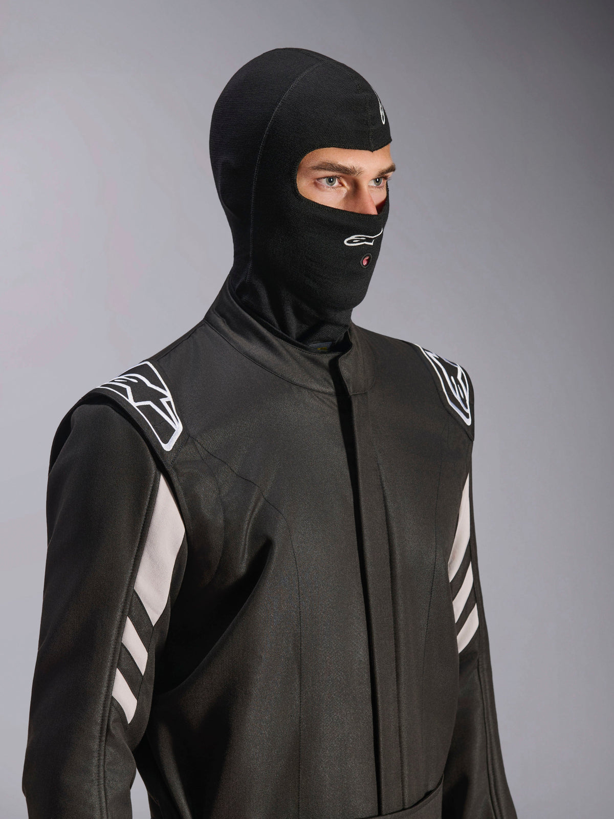 Alpinestars ZX Evo V3 Sturmhaube, Schwarz, feuerfeste Kopfhaube für den Autorennsport, getragen von einem Modell in einem schwarzen Rennanzug mit weißen Akzenten, mit Alpinestars-Logo am Kinn, Öffnung für Hydrationsschlauch, professionelle Motorsport-Schutzausrüstung